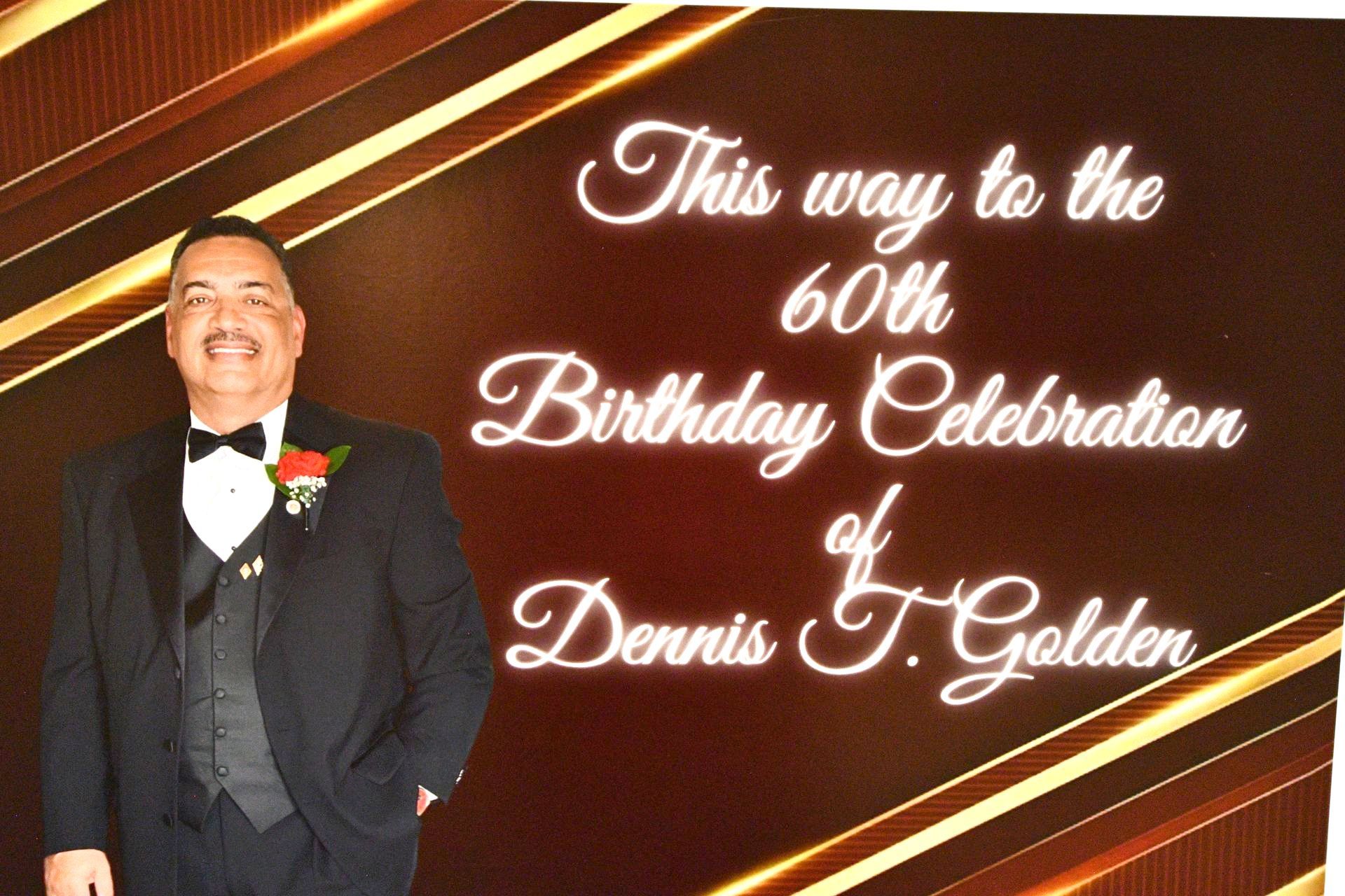 Man in suit smiles, standing by a sign that reads 