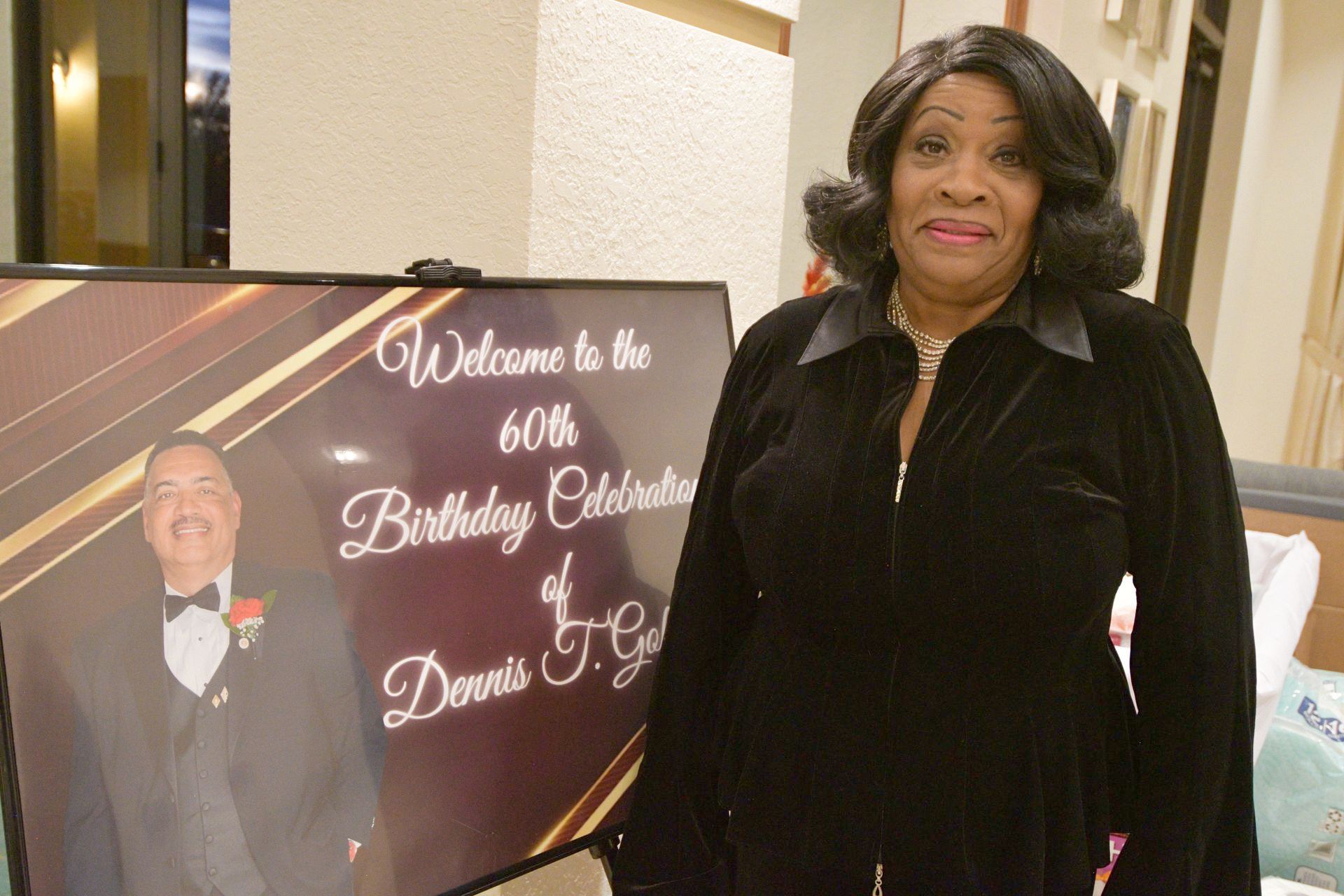 Woman stands near a sign for a 60th birthday celebration with a photo of the celebrant.