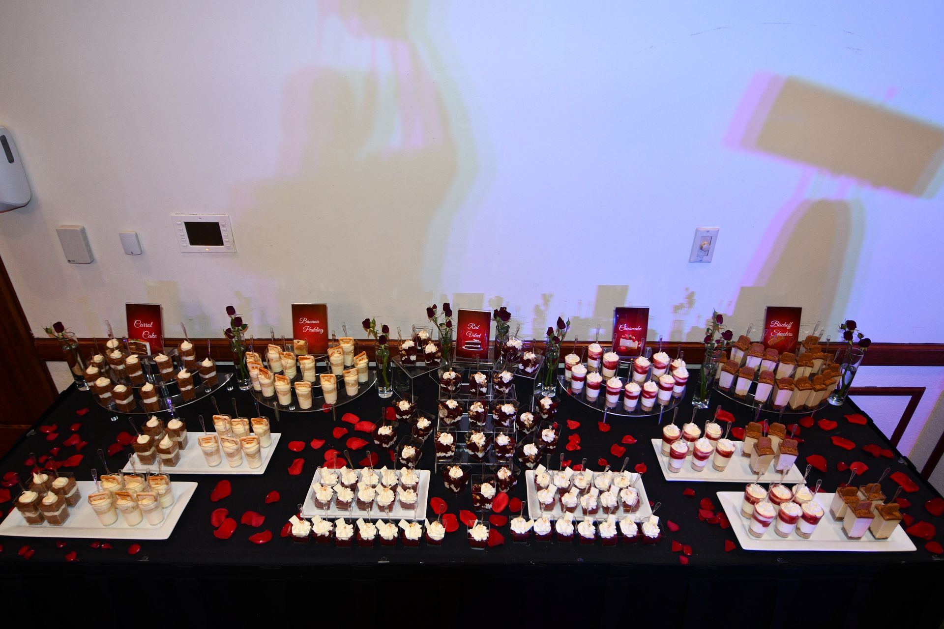 Dessert table with various small treats, rose petals, and a projected image on the wall.