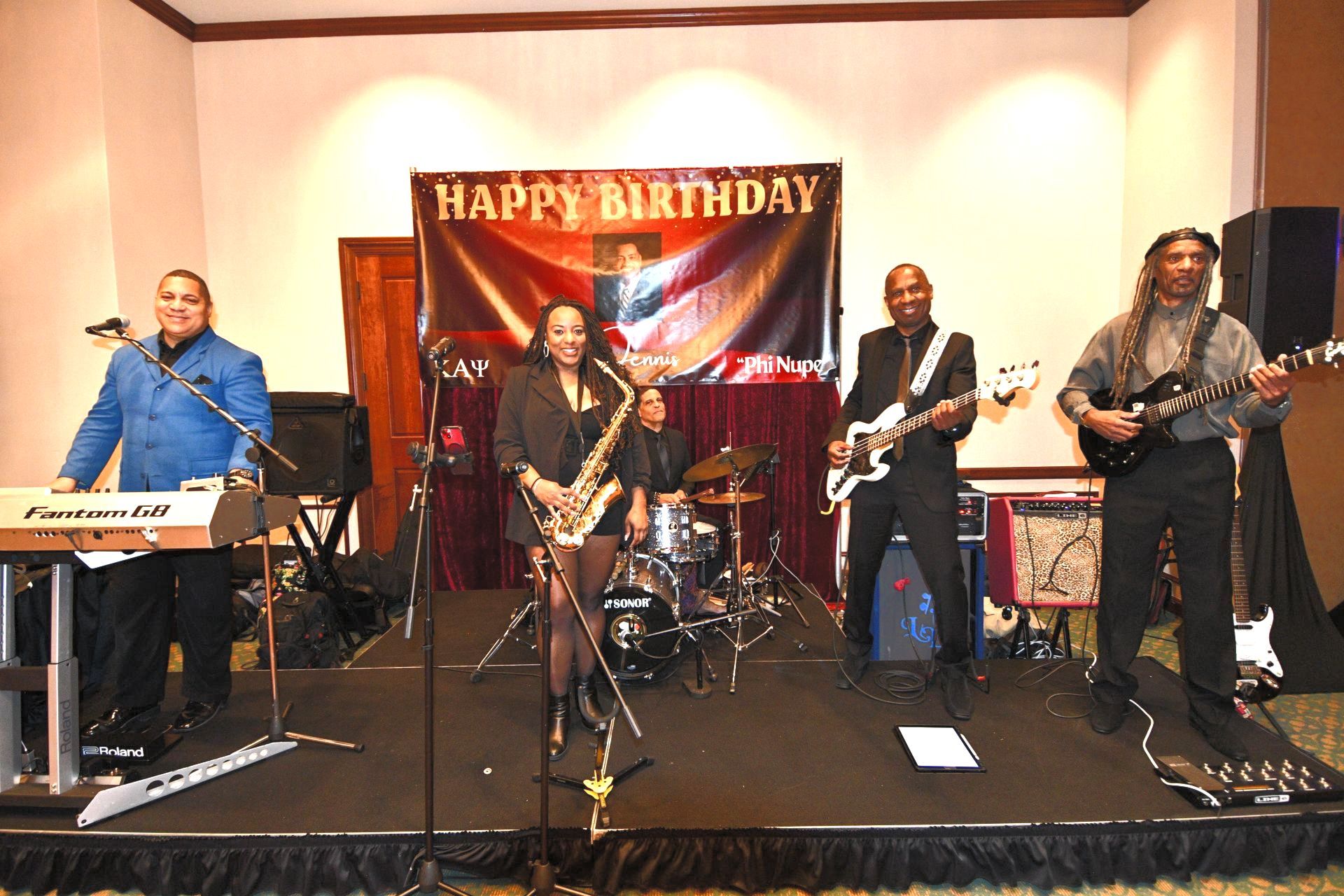 Band performing on stage at a birthday party, with banner and musical instruments.