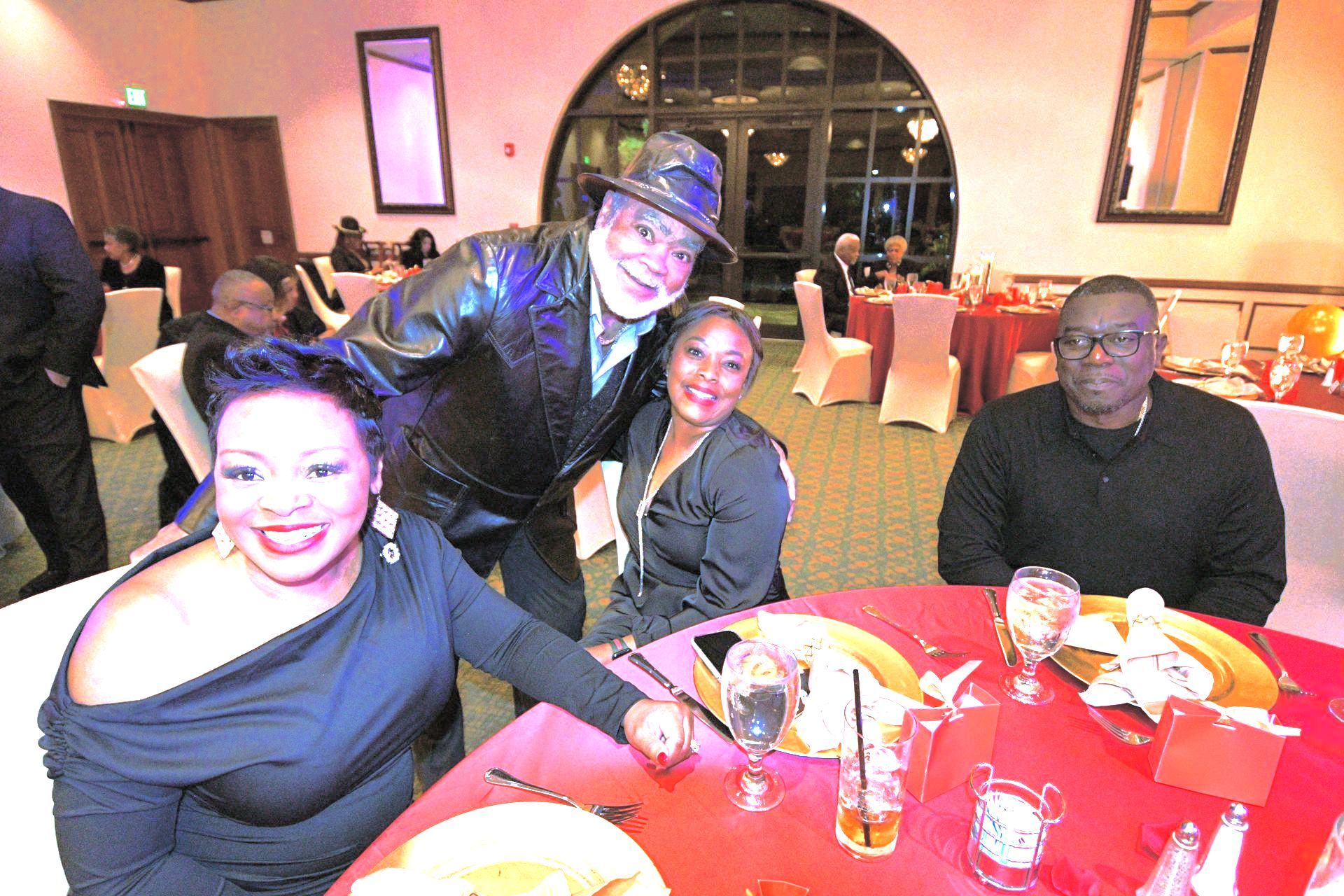 People pose at a formal event, seated at tables with red tablecloths.