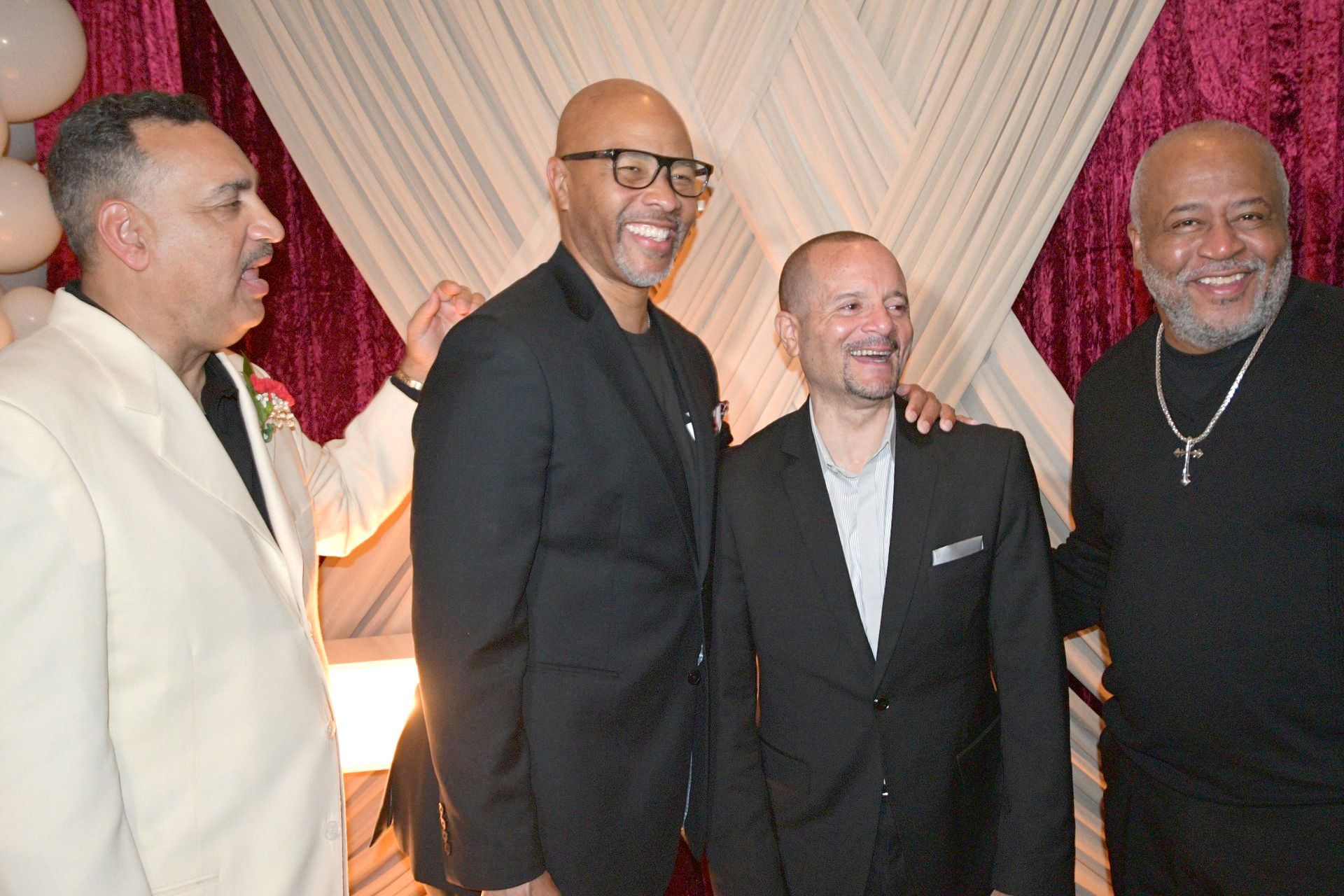 Four men posing together, smiling in front of a draped backdrop.