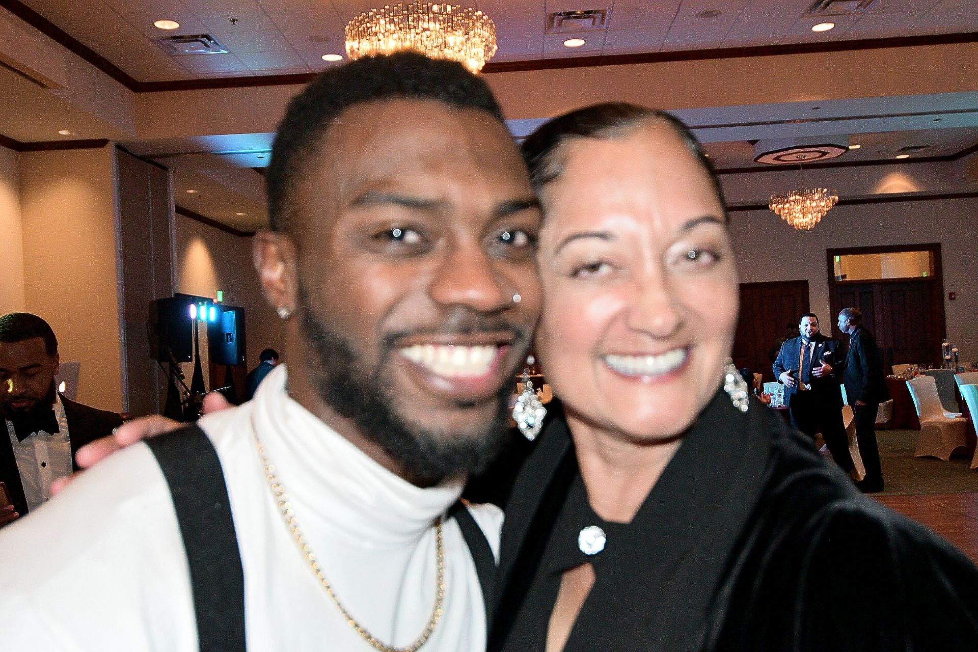 Man and woman smiling, indoors. Man with beard in white shirt. Woman in black clothing, shoulder to shoulder.