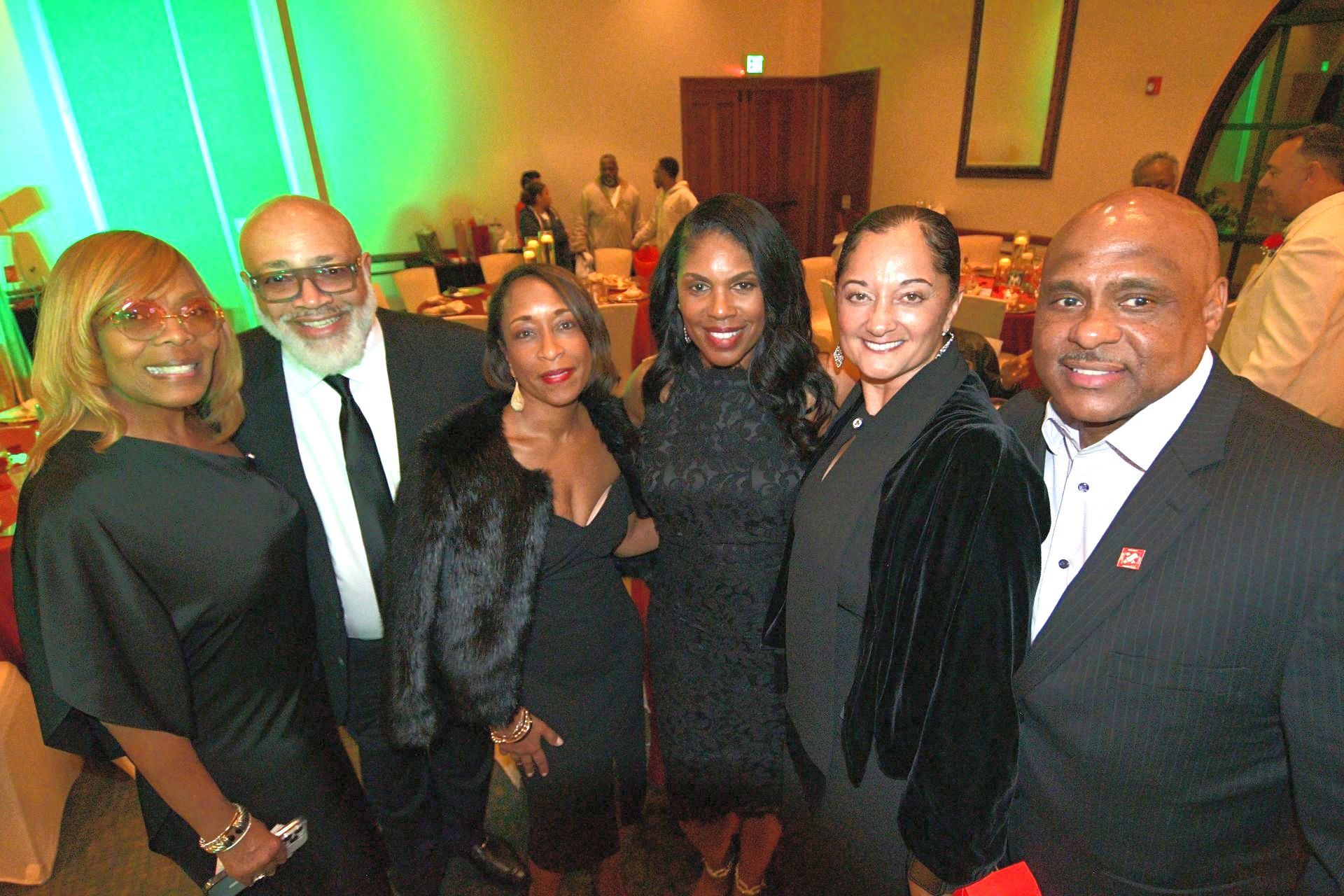 Group of six people smiling at a formal event, lit with green and warm lights.