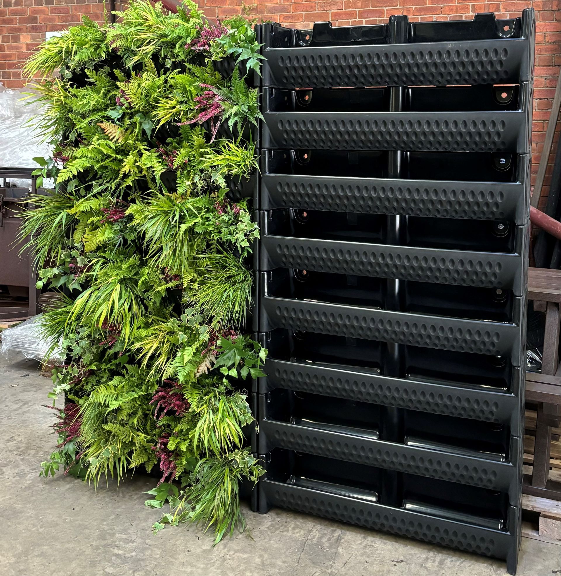 Green wall next to a black vertical planter structure, both on a concrete surface.