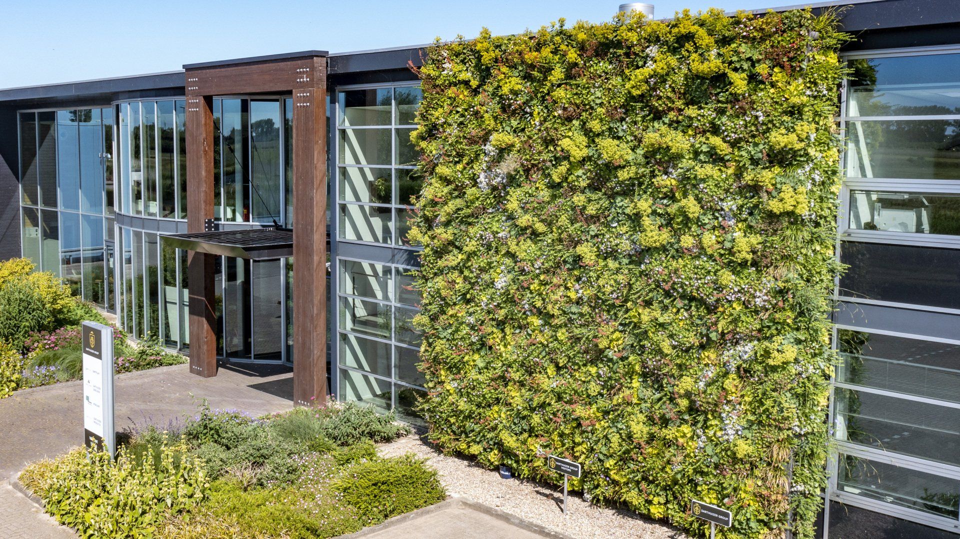 Office building with a large green wall, glass windows, and a landscaped entrance.