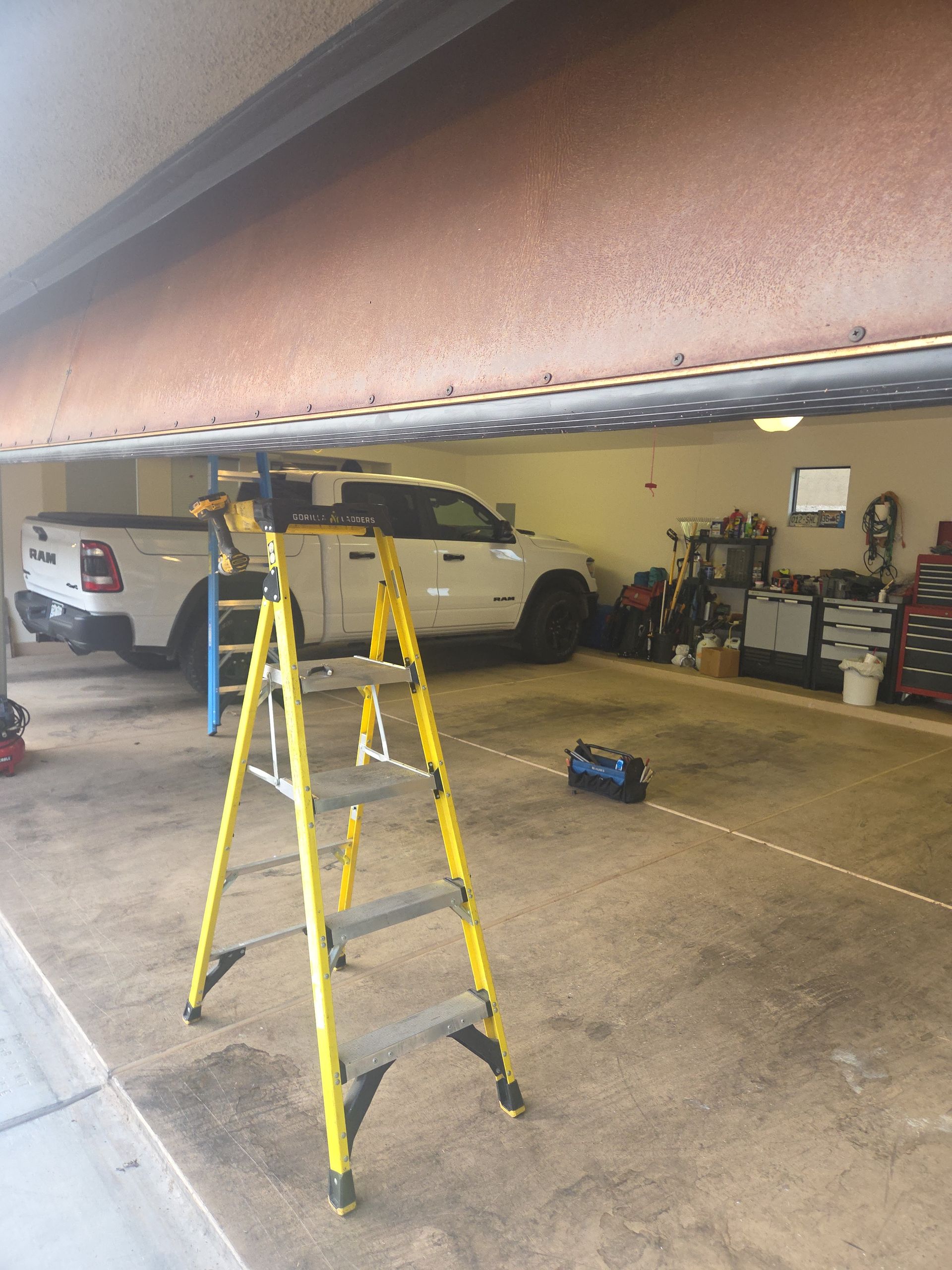 Yellow ladder in a cluttered garage with a white SUV and tools along the back wall.