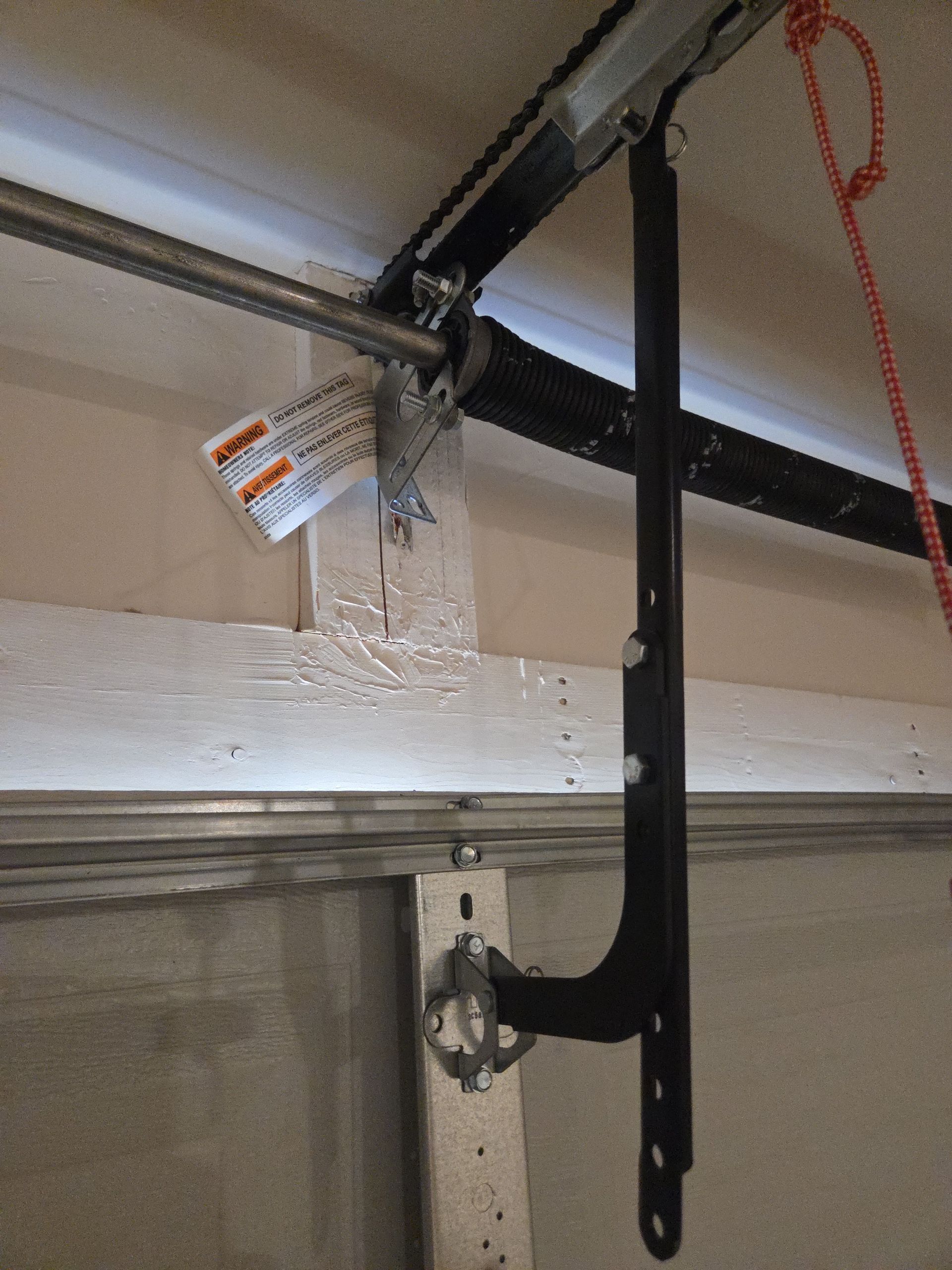 Black garage door opener bracket and rail mounted to a ceiling with a pull cord hanging nearby