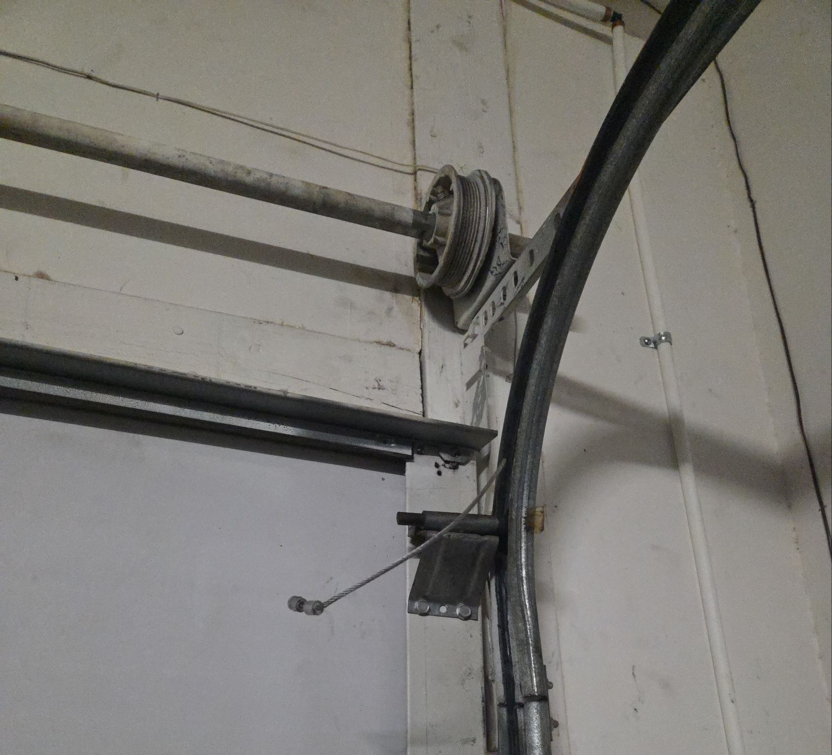 Industrial wall with exposed cables, conduit, and a mounted pulley near the ceiling.