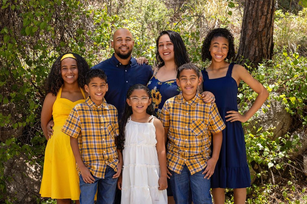 Family of six standing together on a tree-lined dirt path in a wooded area, smiling at the camera.