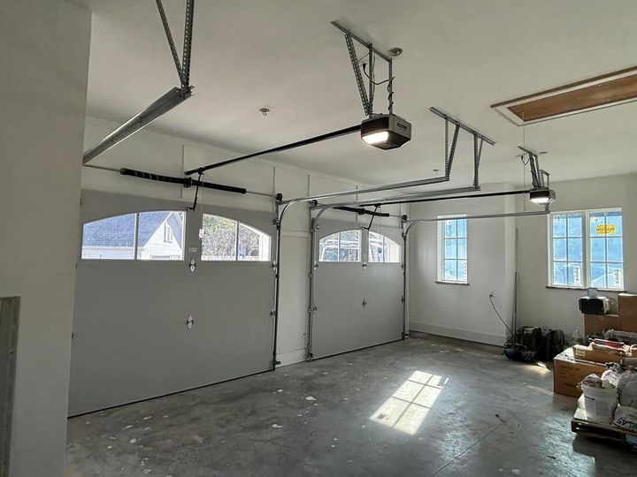 Empty garage interior with white walls, overhead door tracks, windows, and construction materials on the floor