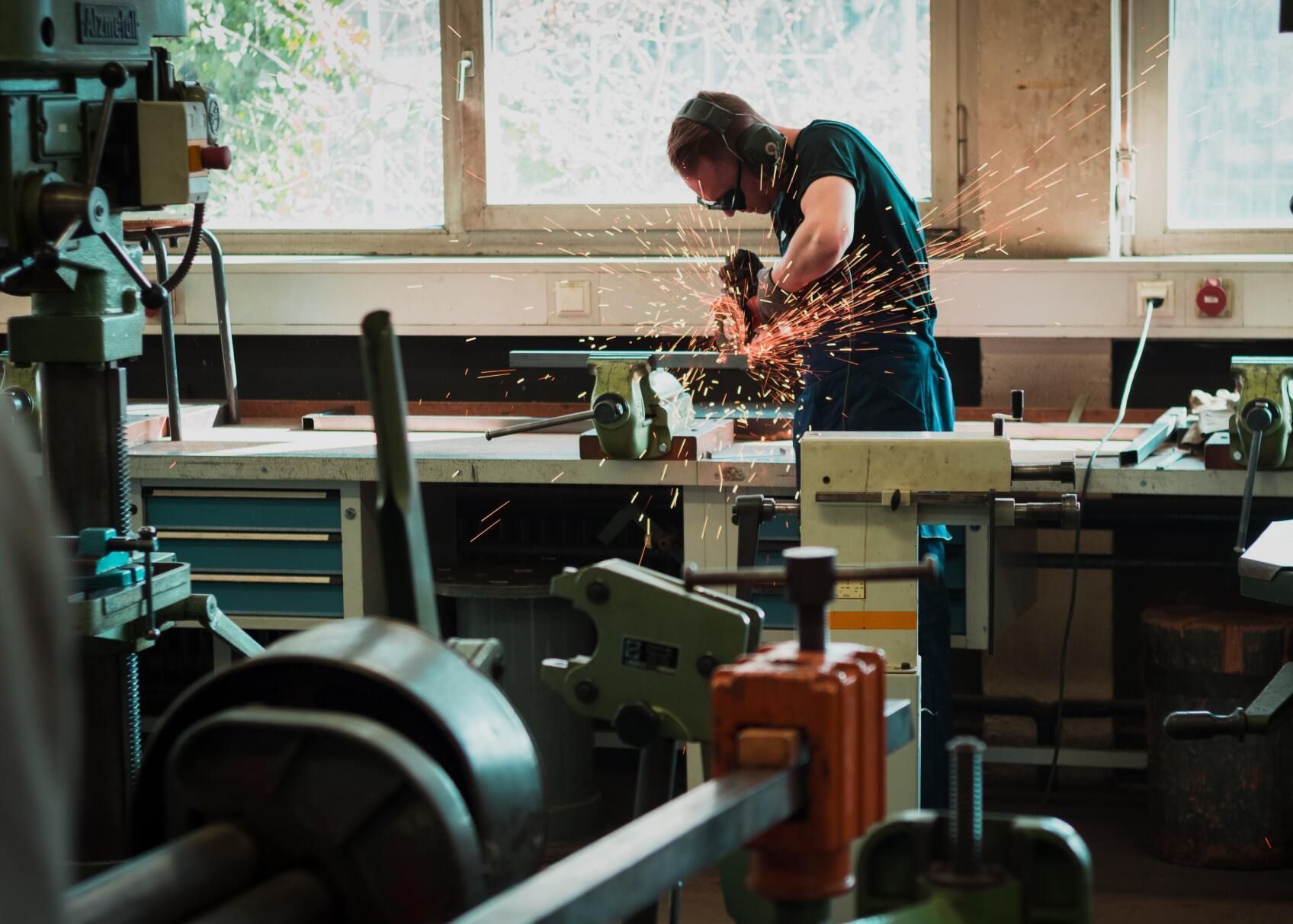 Person working at a cluttered workshop bench, sparks flying from a tool near the window.