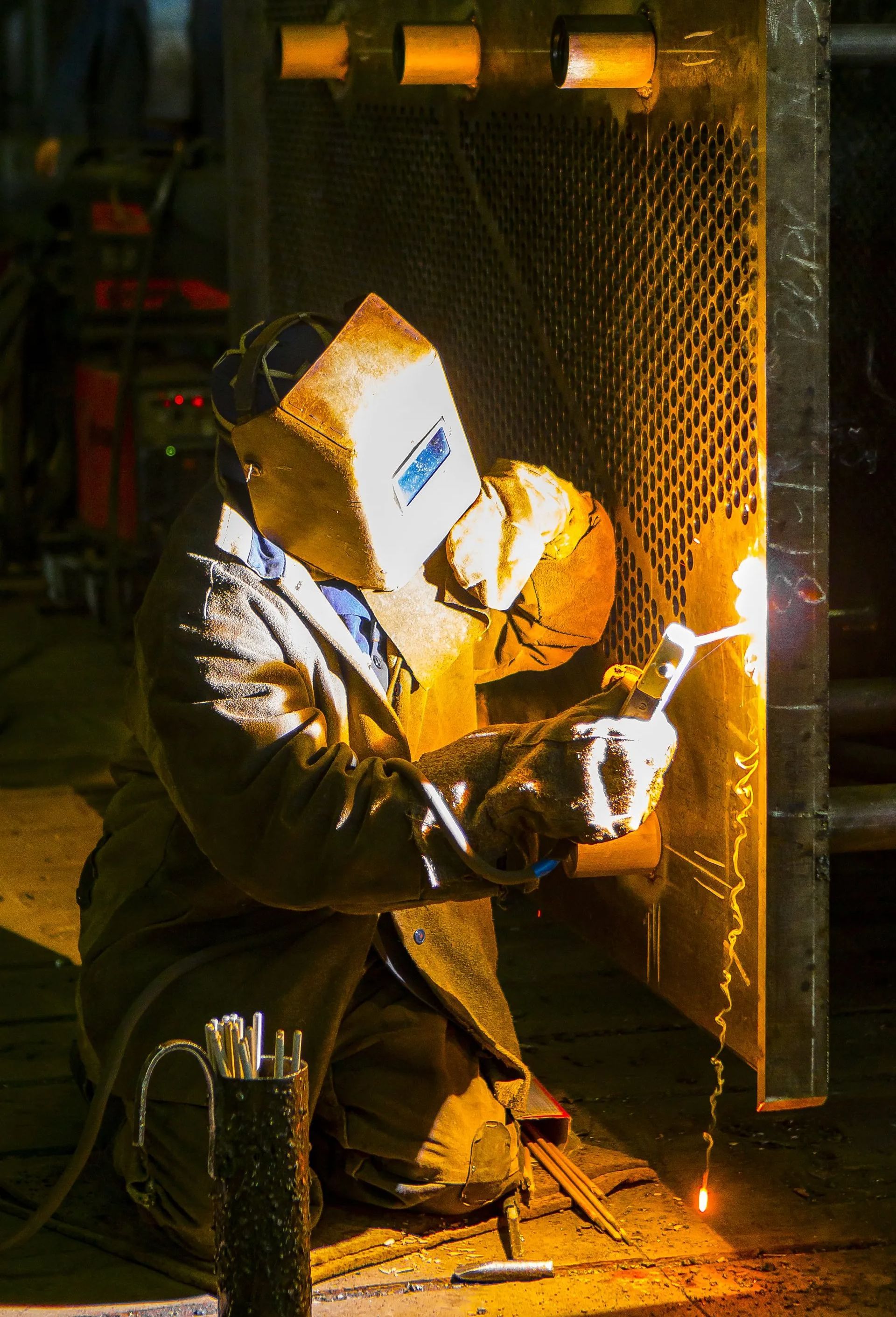 Welder in protective gear working with bright sparks in a dim industrial setting