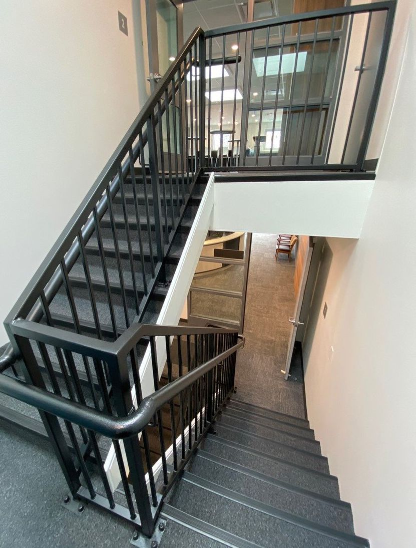 Indoor stairwell with black railings and gray steps connecting two floors.