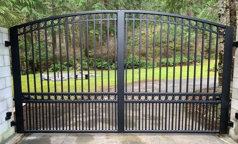 Black metal driveway gate in front of a grassy yard and trees.