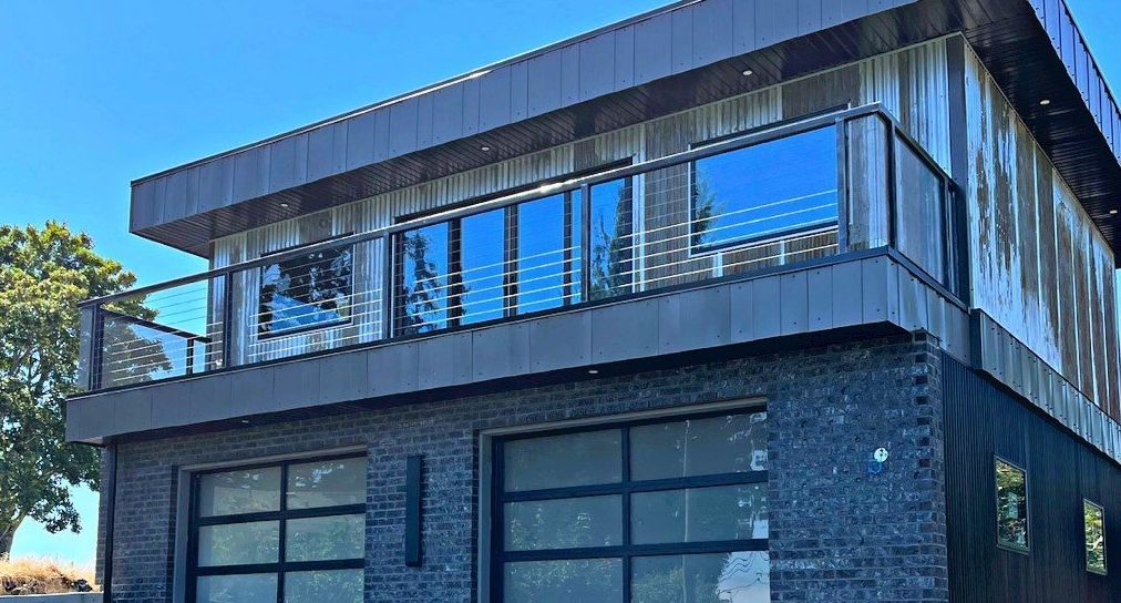 Modern two-story dark brick house with large glass windows and a balcony in bright daylight