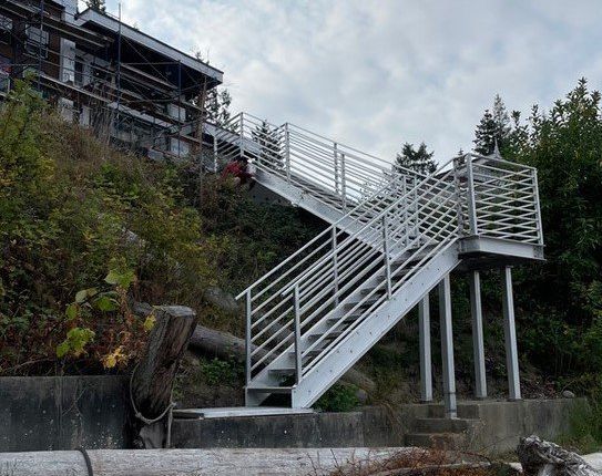 Steep white stairway and ramp beside a rocky shoreline, leading up to a building on a bluff