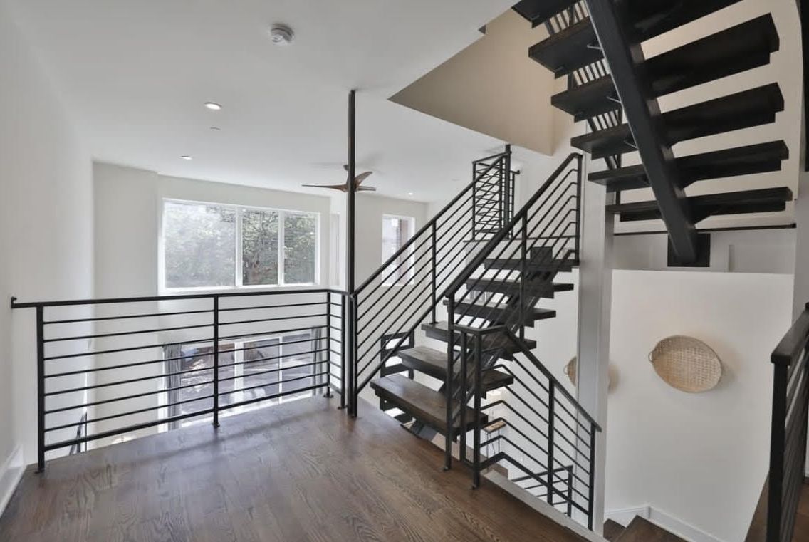 Modern interior with staircase, black railings, and large window in a bright loft-style space