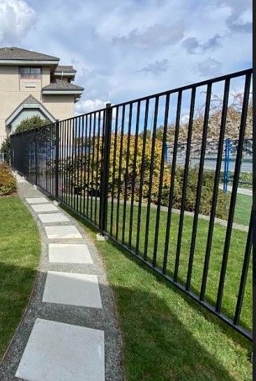 Black metal fence beside a curved stone path and green lawn outside a building.