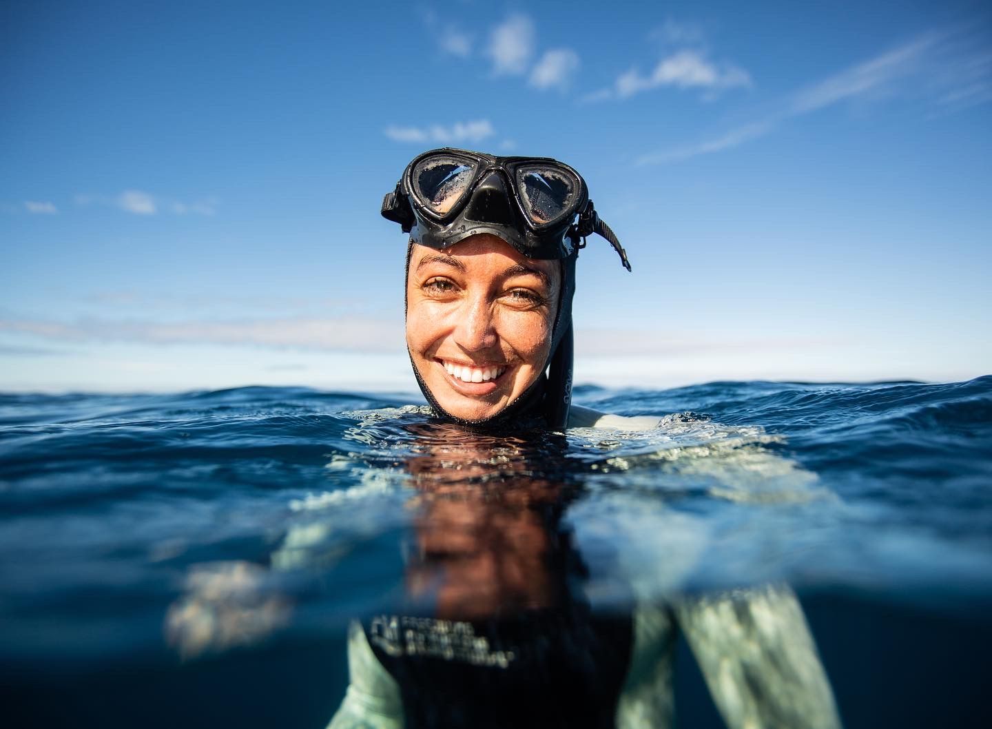 A woman is smiling while freediving in the ocean.