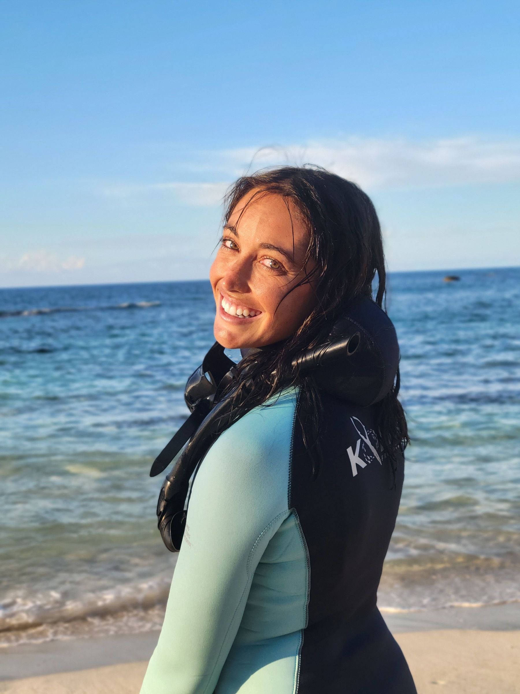 A woman in a wetsuit is standing on a beach near the ocean.