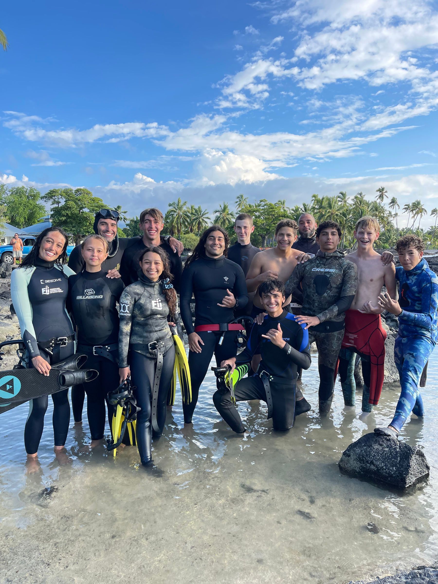 A group of people in wet suits are posing for a picture on the beach.