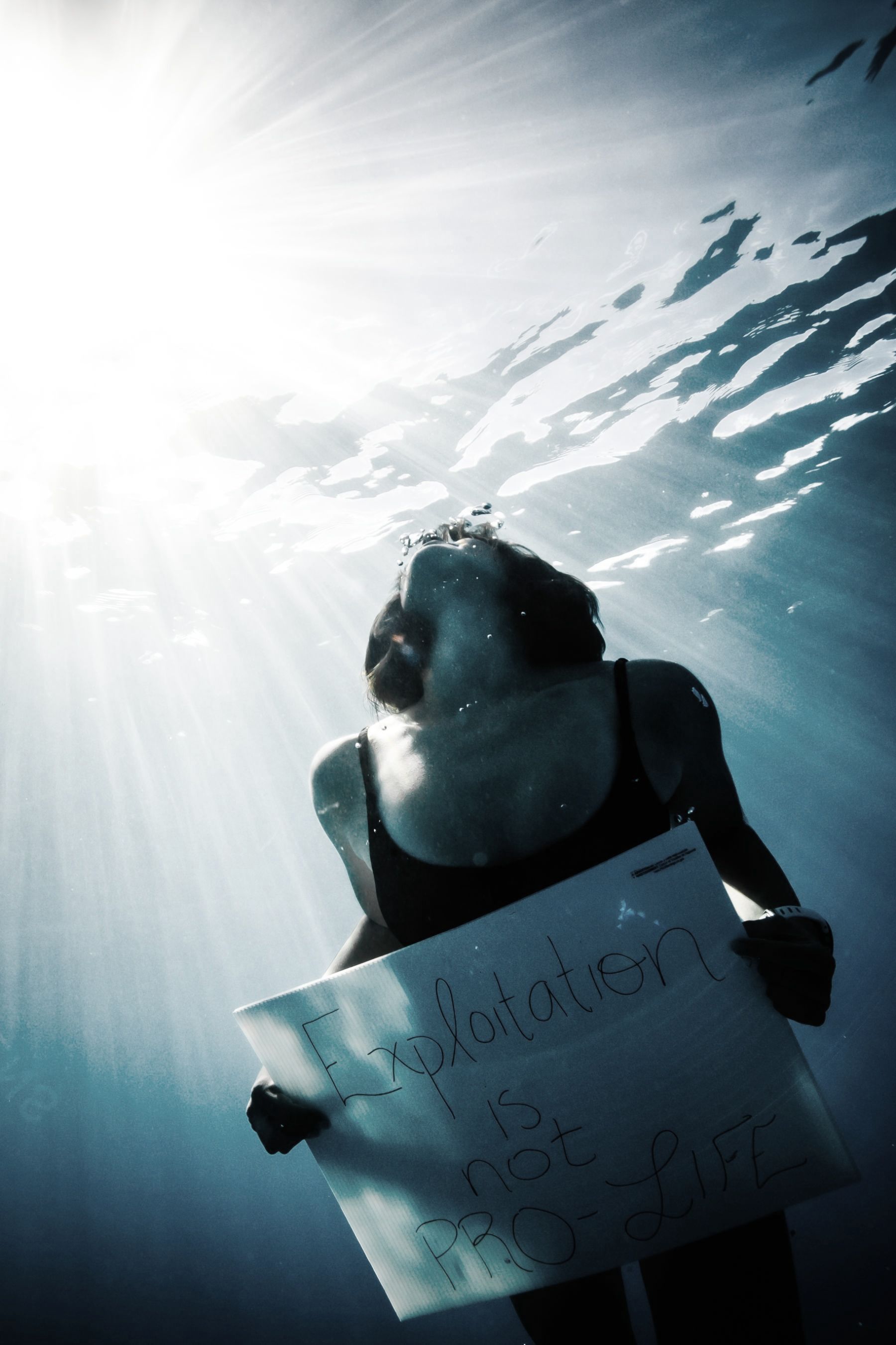 A woman is underwater holding a sign that says