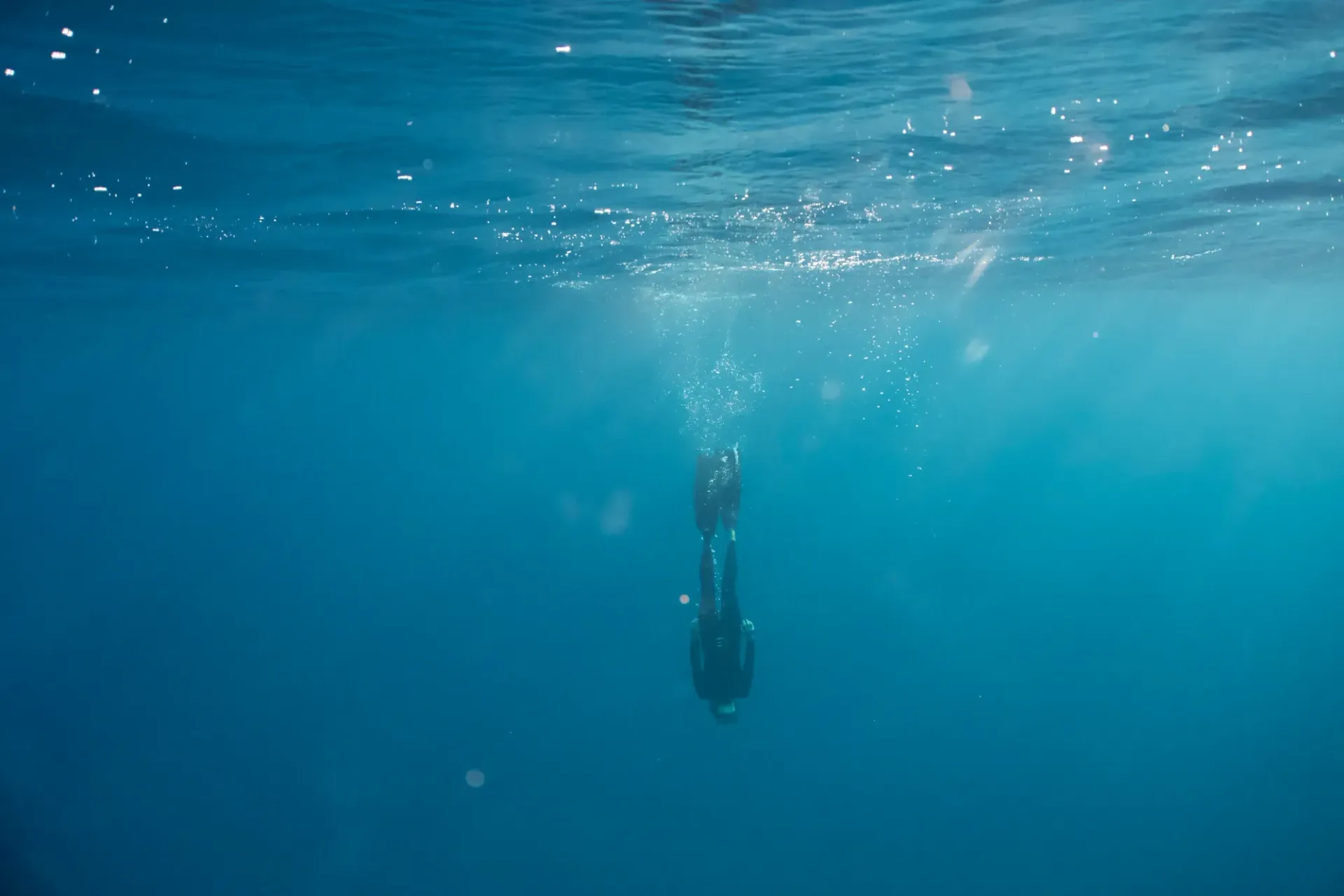 A person is freediving in the ocean with bubbles coming out of the water.