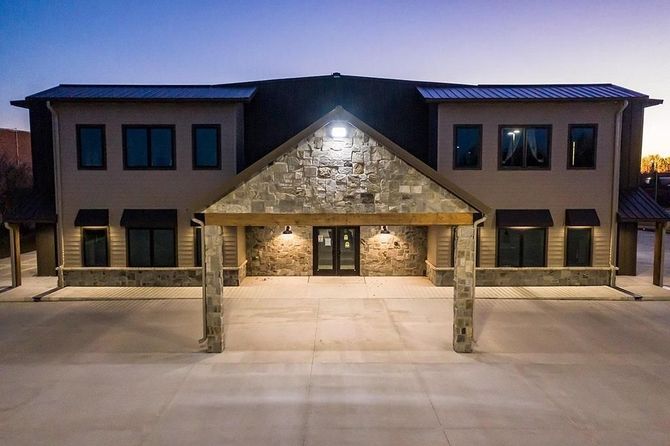 Front view of a modern two-story building with stone entrance and lit facade at dusk