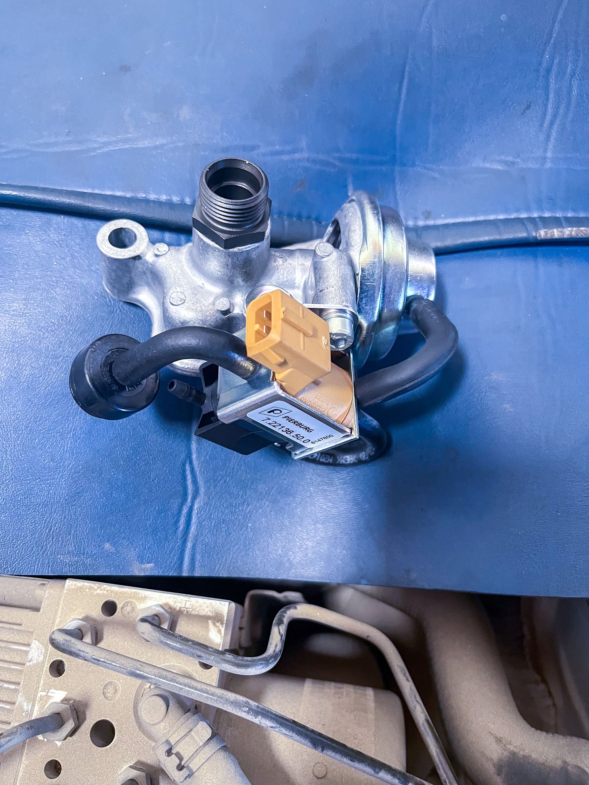 A car part with an orange connector, tubes, and metal components, on a blue surface, with car chassis visible below. | Jim Brangham Auto Repair