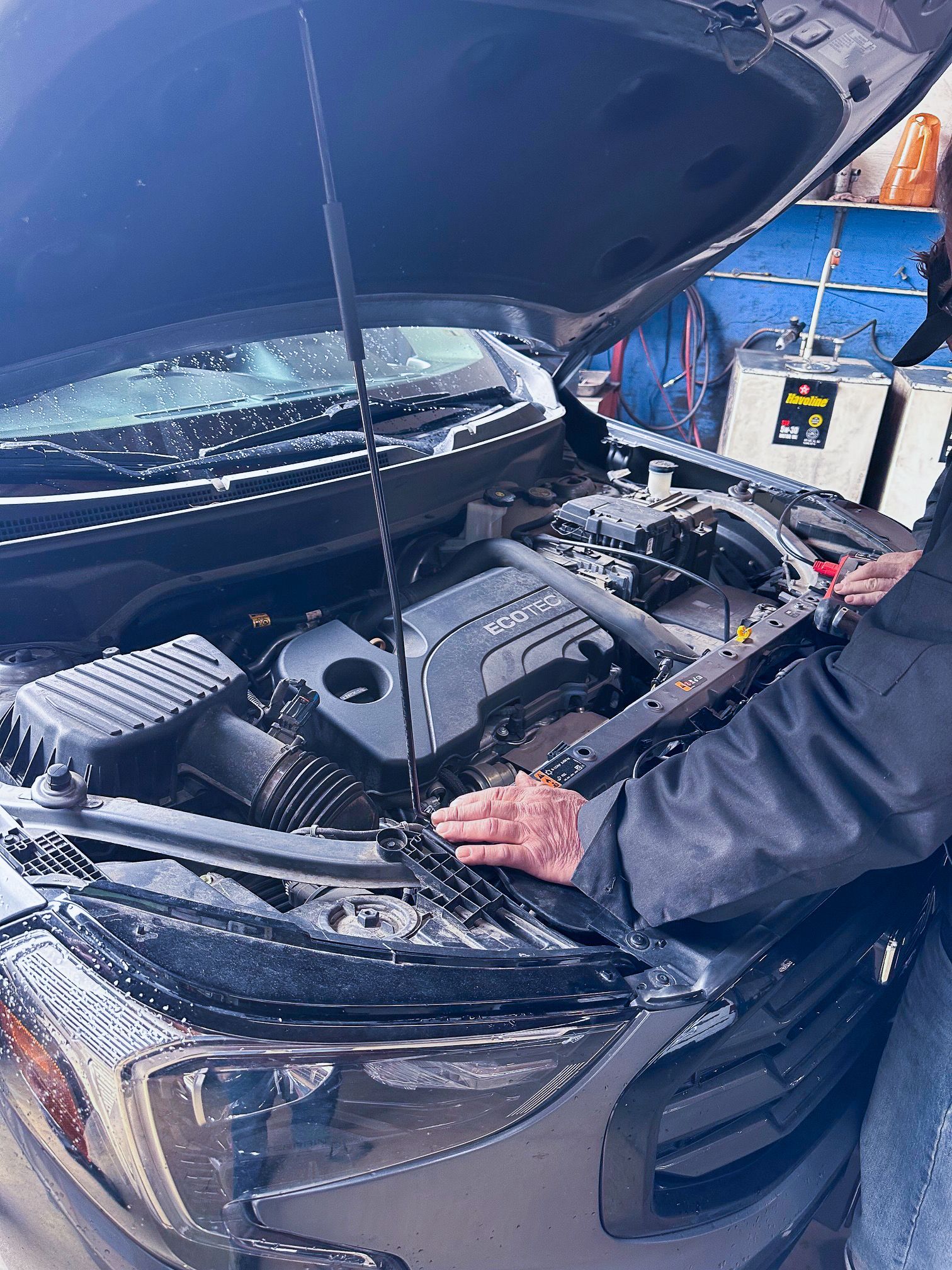 Person inspecting the engine of a gray car with the hood up at an auto shop. | Jim Brangham Auto Repair