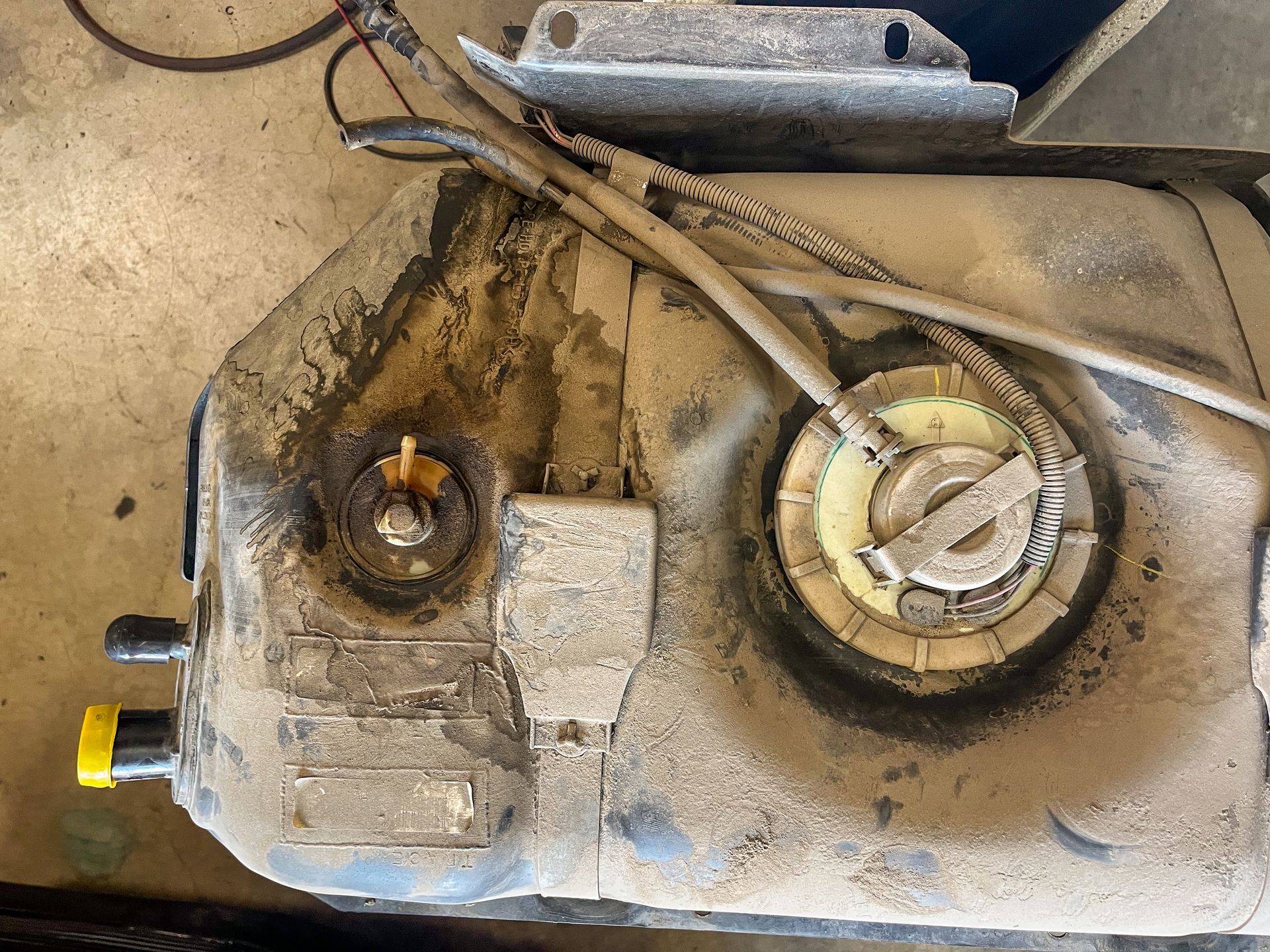Fuel tank covered in dirt, with fuel lines and filler neck visible. | Jim Brangham Auto Repair