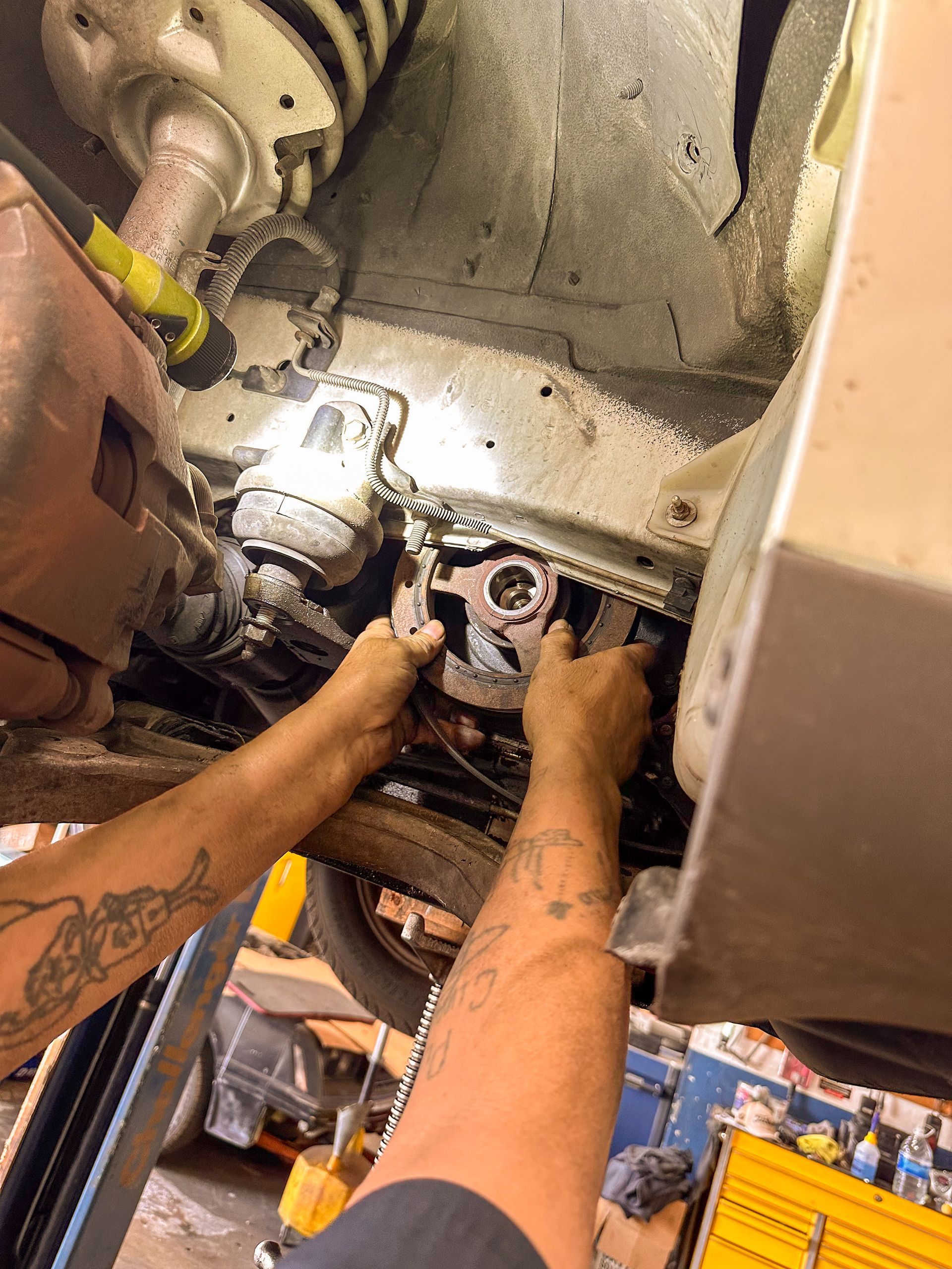 Mechanic working on car underside, focusing on suspension and exhaust components in a garage. | Jim Brangham Auto Repair