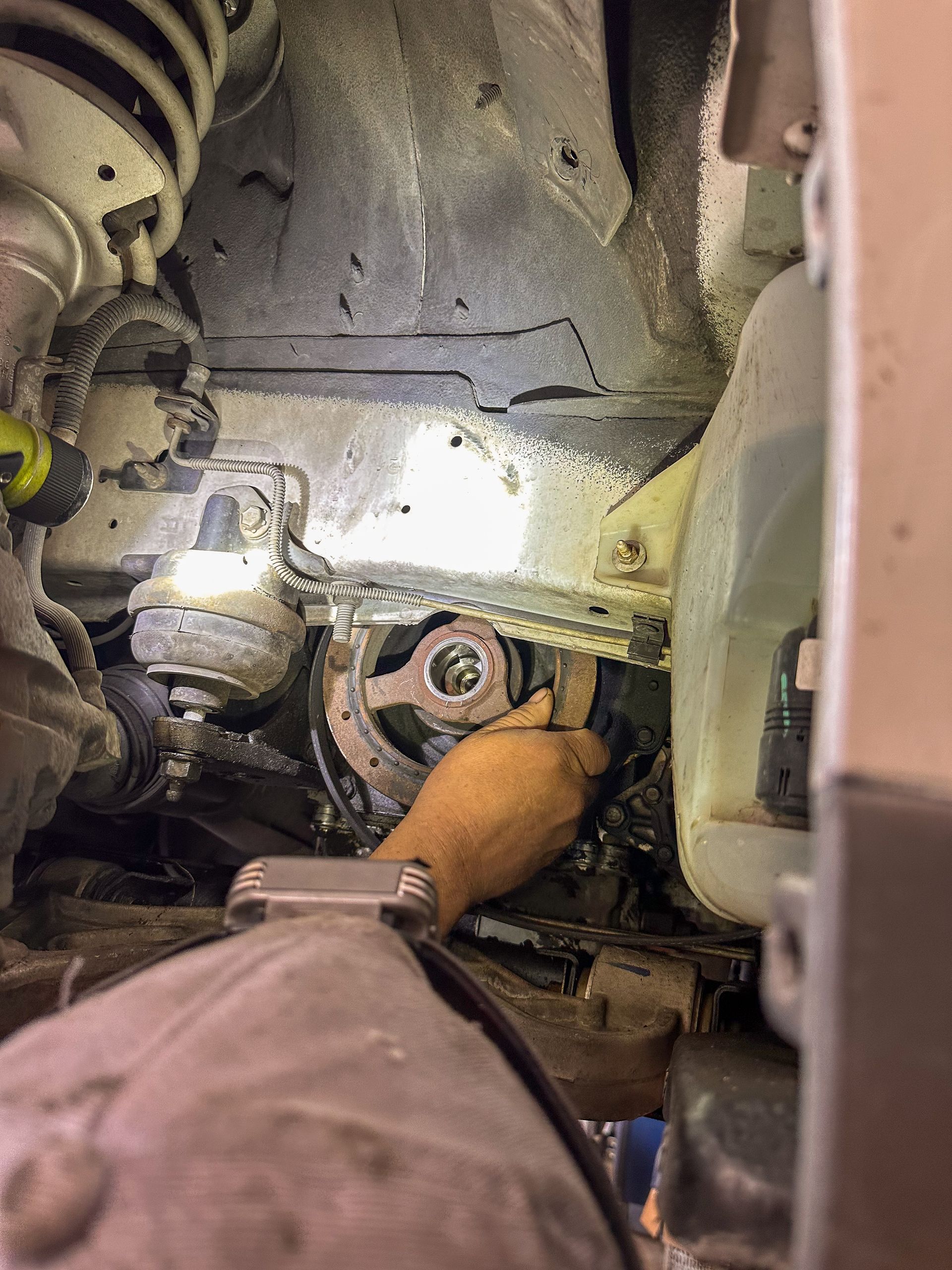 A mechanic's gloved hand working on a car's undercarriage; wrenching near a wheel hub. | Jim Brangham Auto Repair
