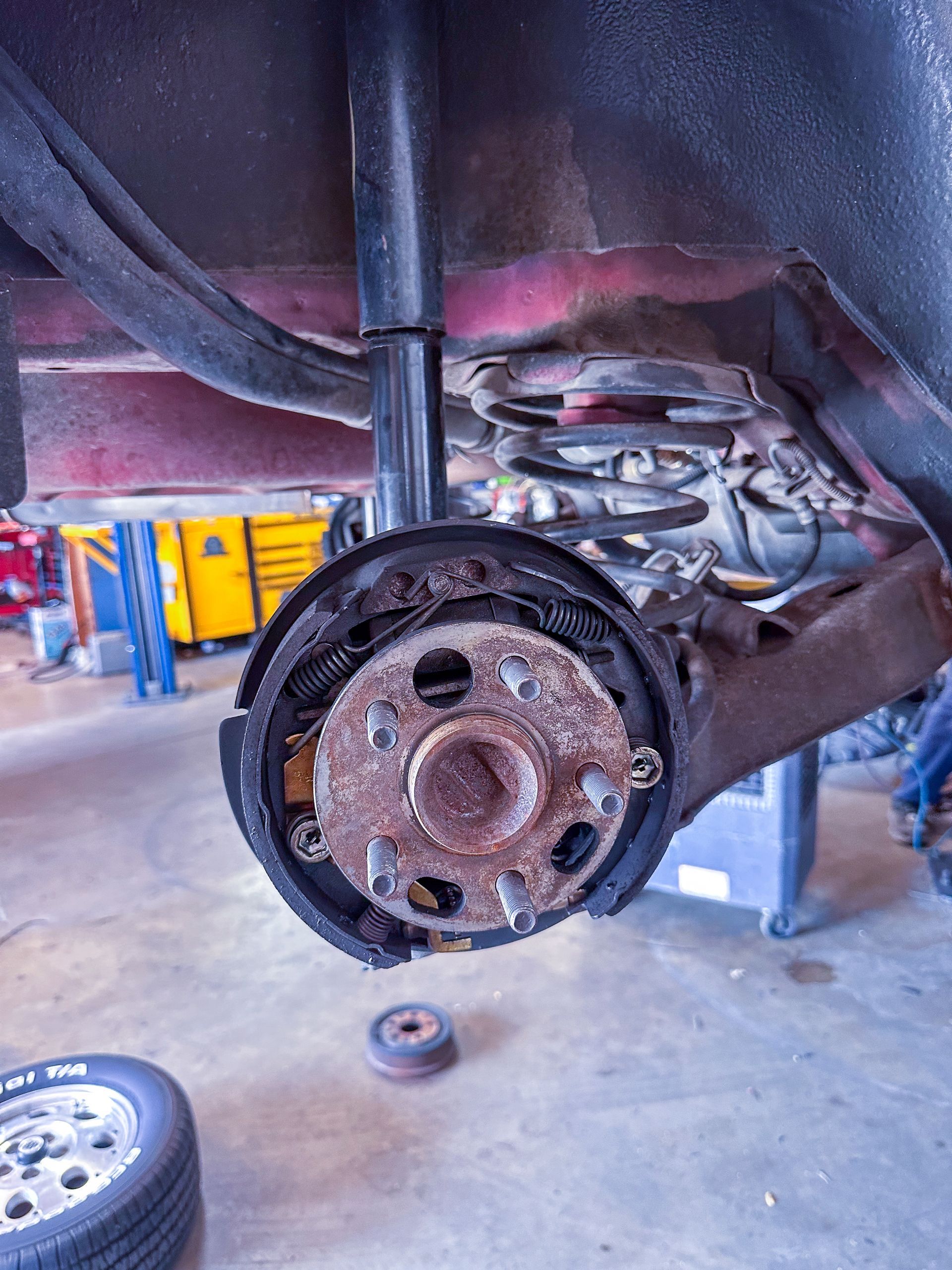 Rear car wheel assembly with exposed brake components, rusty hub, and red body frame. | Jim Brangham Auto Repair