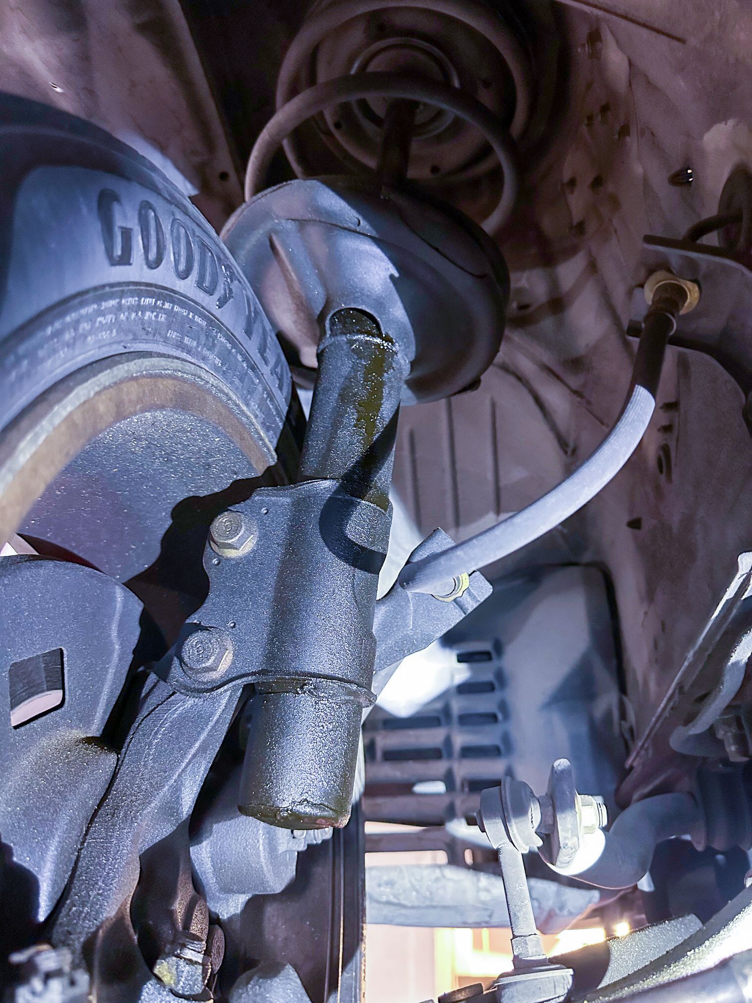 Leaking vehicle strut and brake assembly, close-up. Black and dark grey with a tire in the background. | Jim Brangham Auto Repair