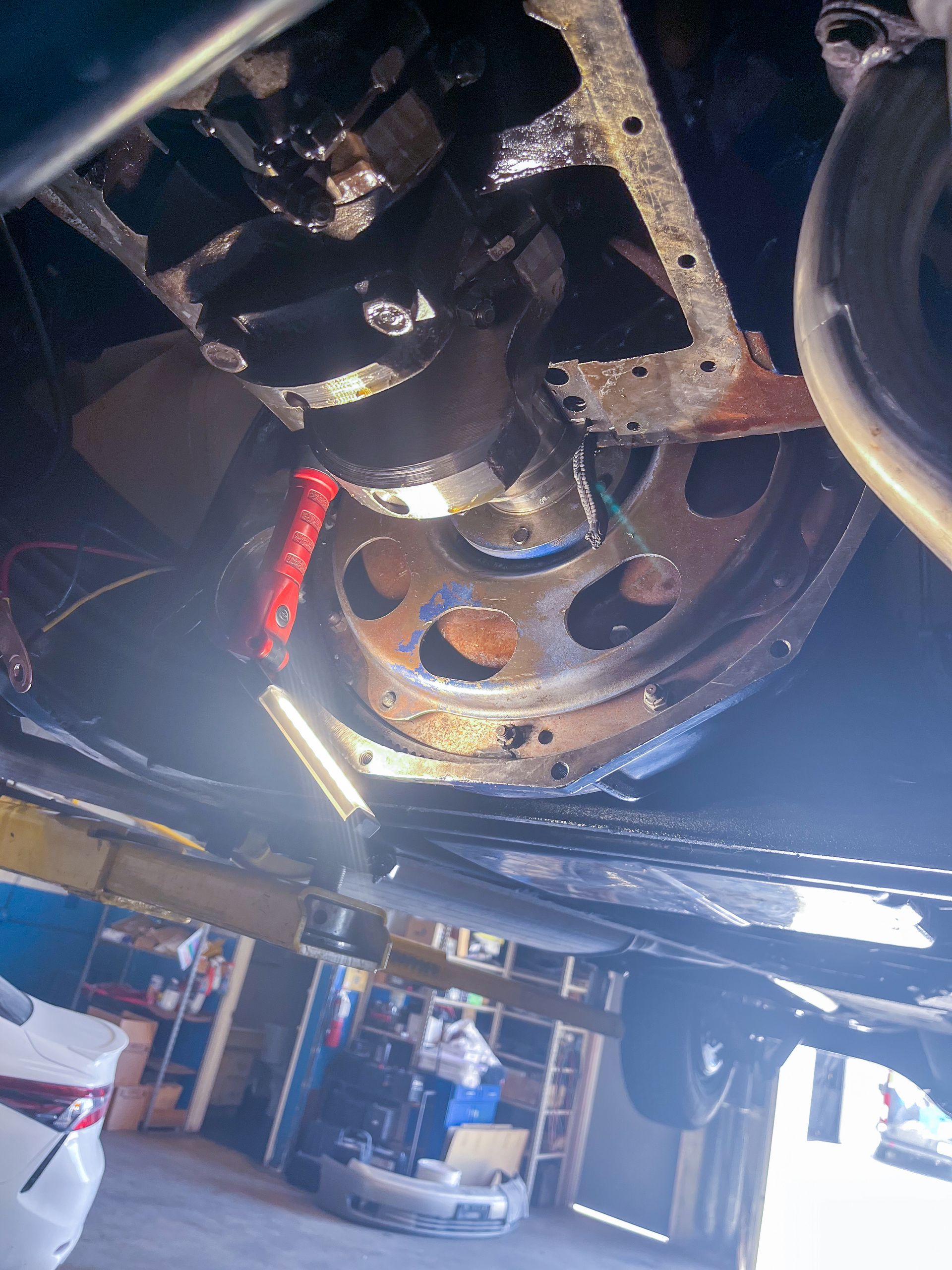 Underside of a vehicle; visible engine components, oil pan. Crankshaft, flywheel; mechanic's bay setting. | Jim Brangham Auto Repair
