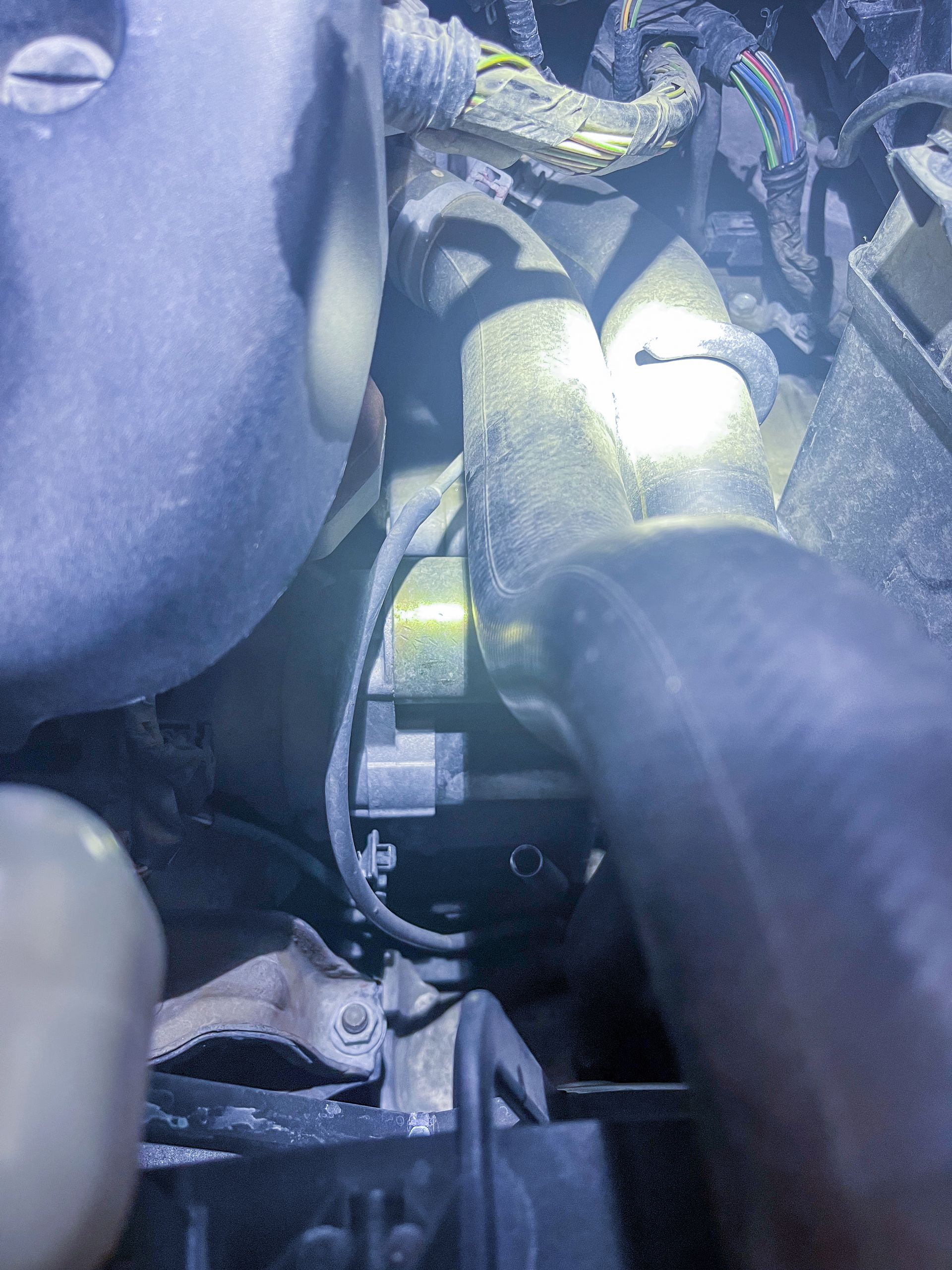 Engine bay, illuminated by a flashlight. Wires, hoses, and other components are visible, possibly for automotive repair. | Jim Brangham Auto Repair