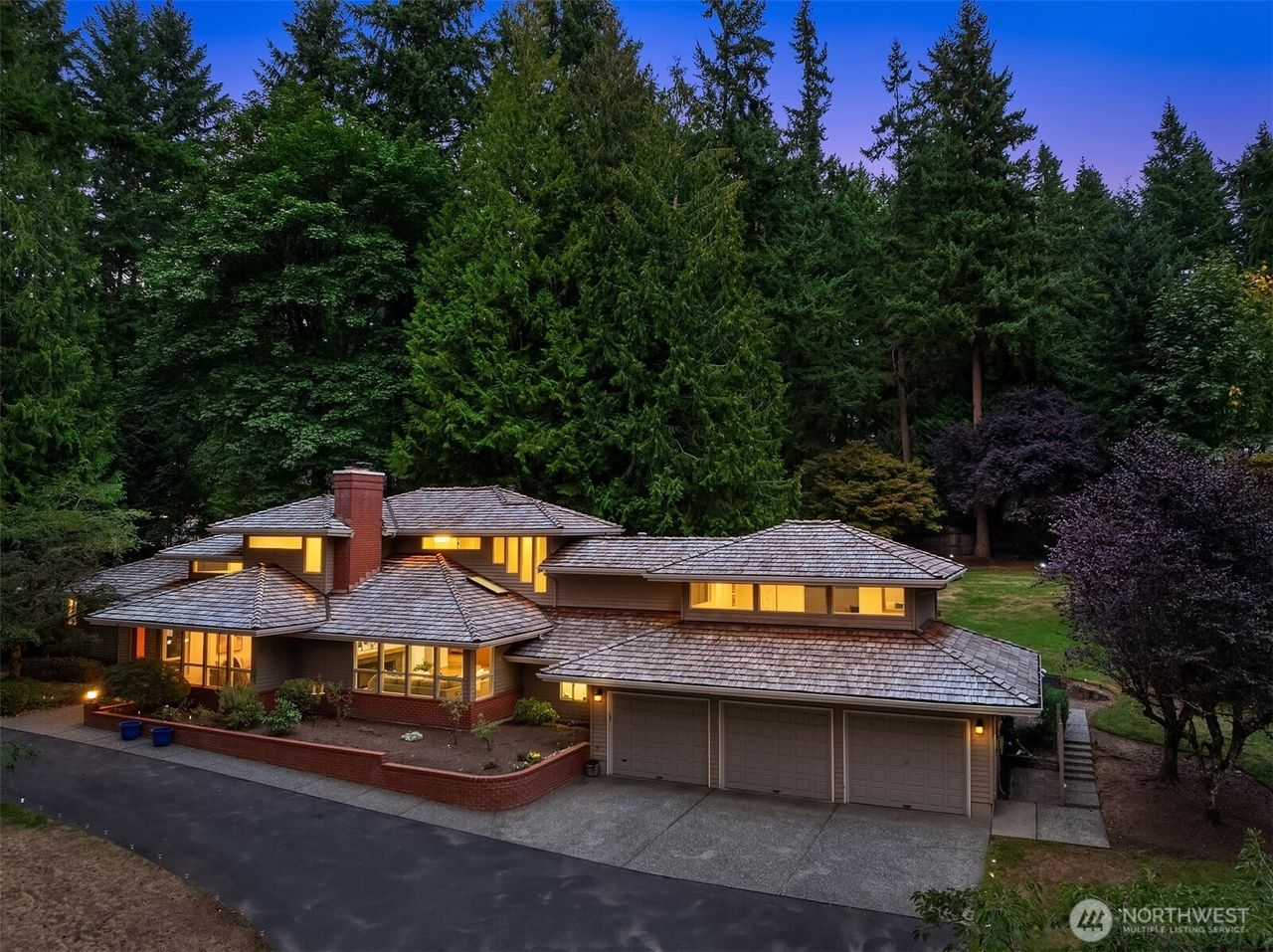 A luxury home with a cedar shake roof, nestled amidst tall evergreen trees, driveway in foreground.