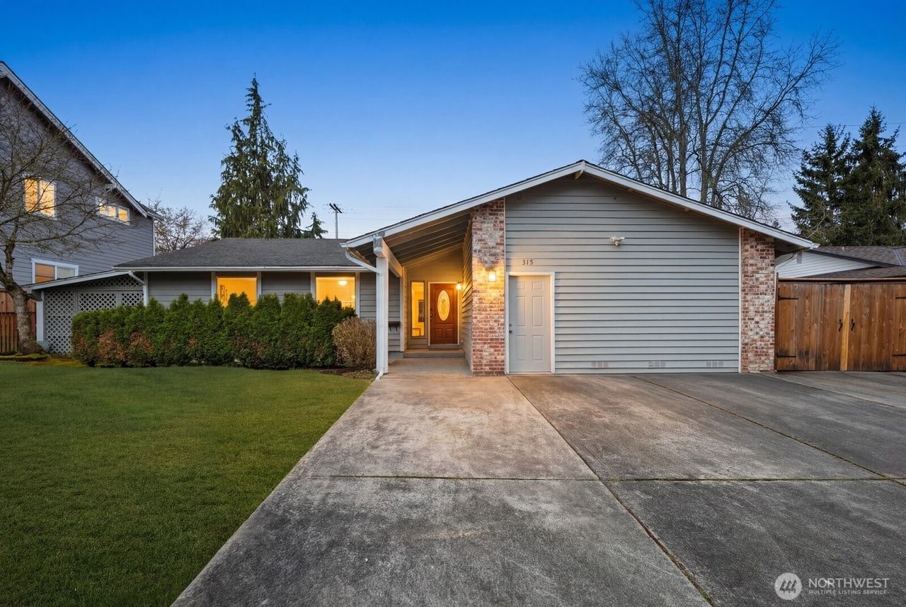 Suburban house at dusk with lit porch, driveway, and attached garage with white door