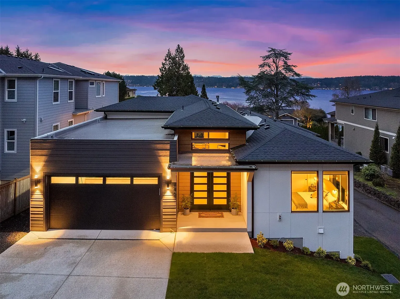 An aerial view of a Sammamish lake house with a garage and a view of a lake at sunset.