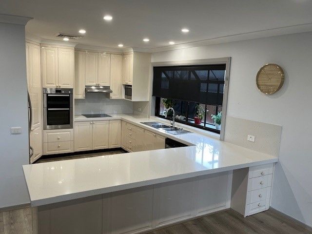 Cream-colored modern kitchen with a large white countertop, stainless steel appliances, and a window with a dark shade — Wards Kitchens in Berkeley Vale, NSW