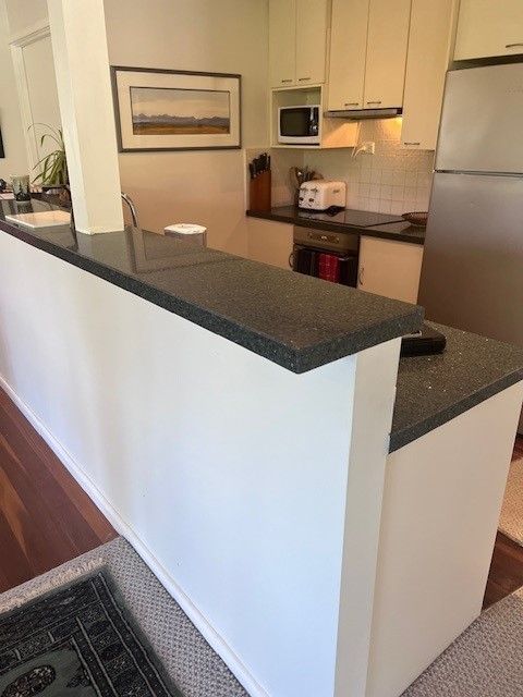 Kitchen with white cabinets, dark countertop, microwave, and stainless steel refrigerator — Wards Kitchens in Berkeley Vale, NSW