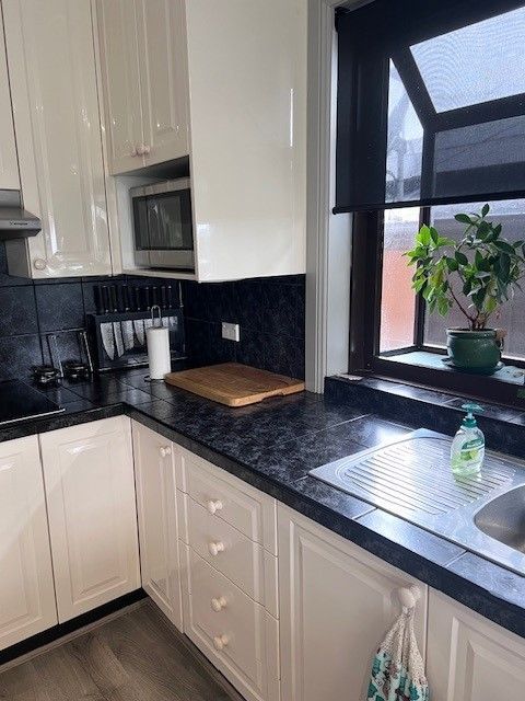 Cream kitchen with black countertops, microwave, sink, and window with a plant — Wards Kitchens in Berkeley Vale, NSW