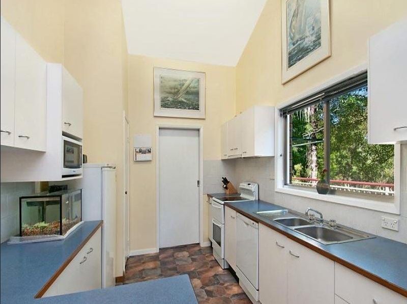 Kitchen with blue countertops, white cabinets, stainless steel sink, and a window overlooking greenery — Wards Kitchens in Berkeley Vale, NSW