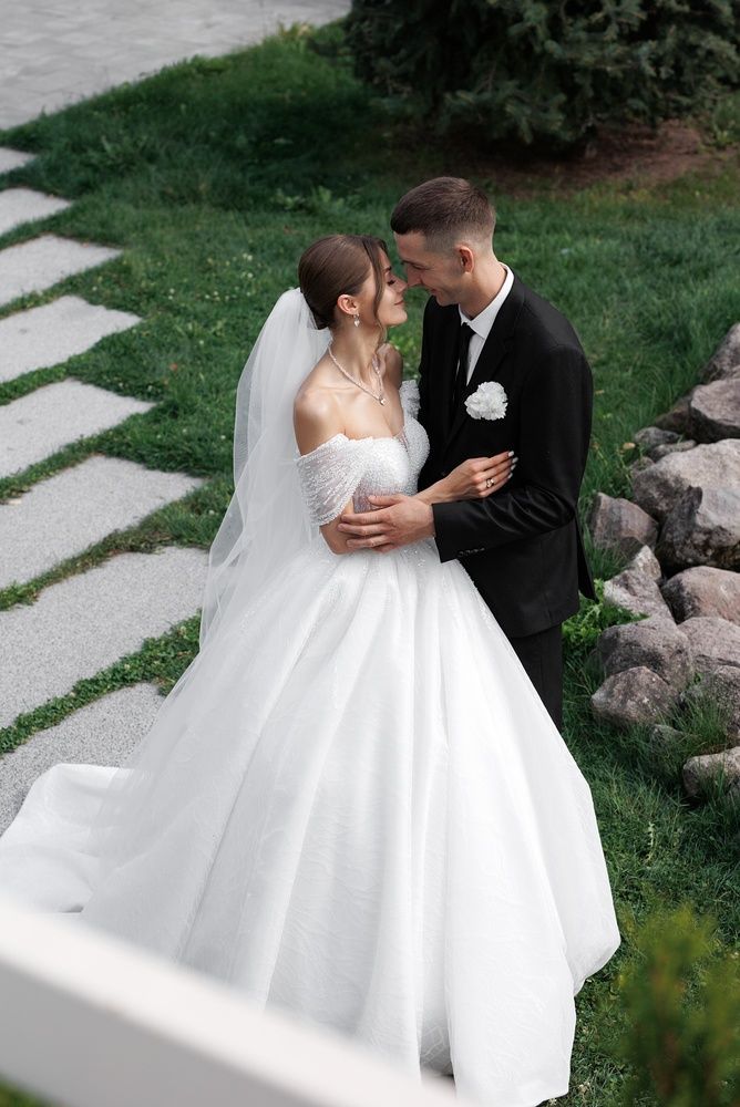 Bride and groom in wedding attire sharing a kiss on a garden path