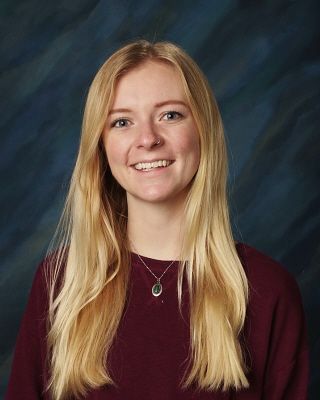 A young woman with long blonde hair is wearing a maroon sweater and a necklace.