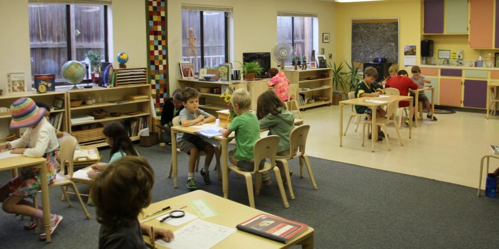 A group of children are sitting at tables in a  montessori classroom