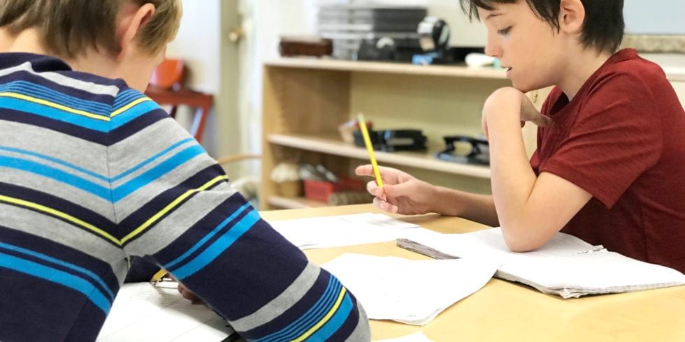Two young boys are sitting at a table with pencils in their hands.