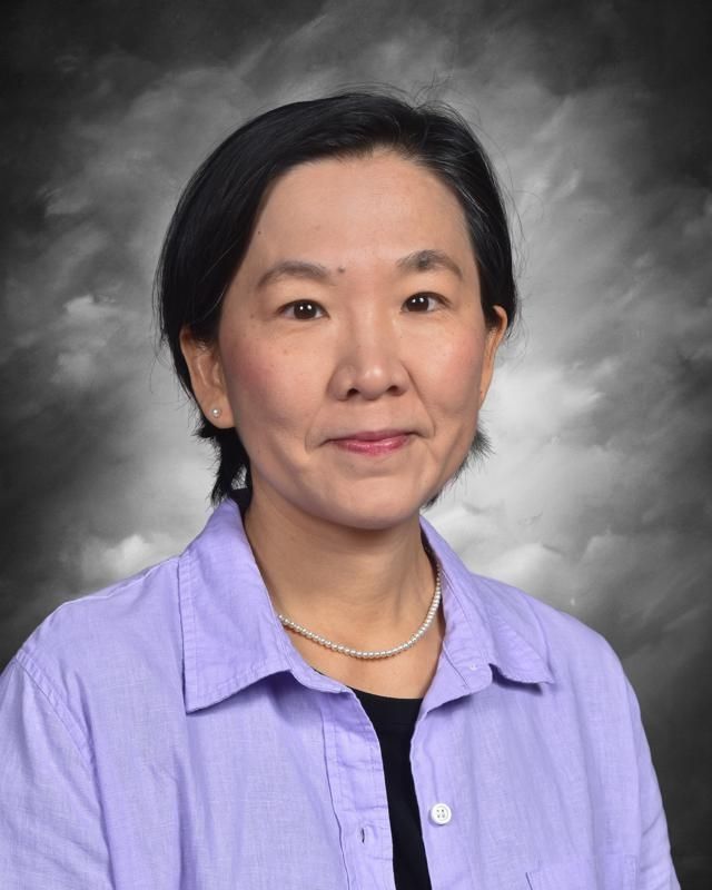 A woman in a red sweater and black vest is standing in front of a blue background.